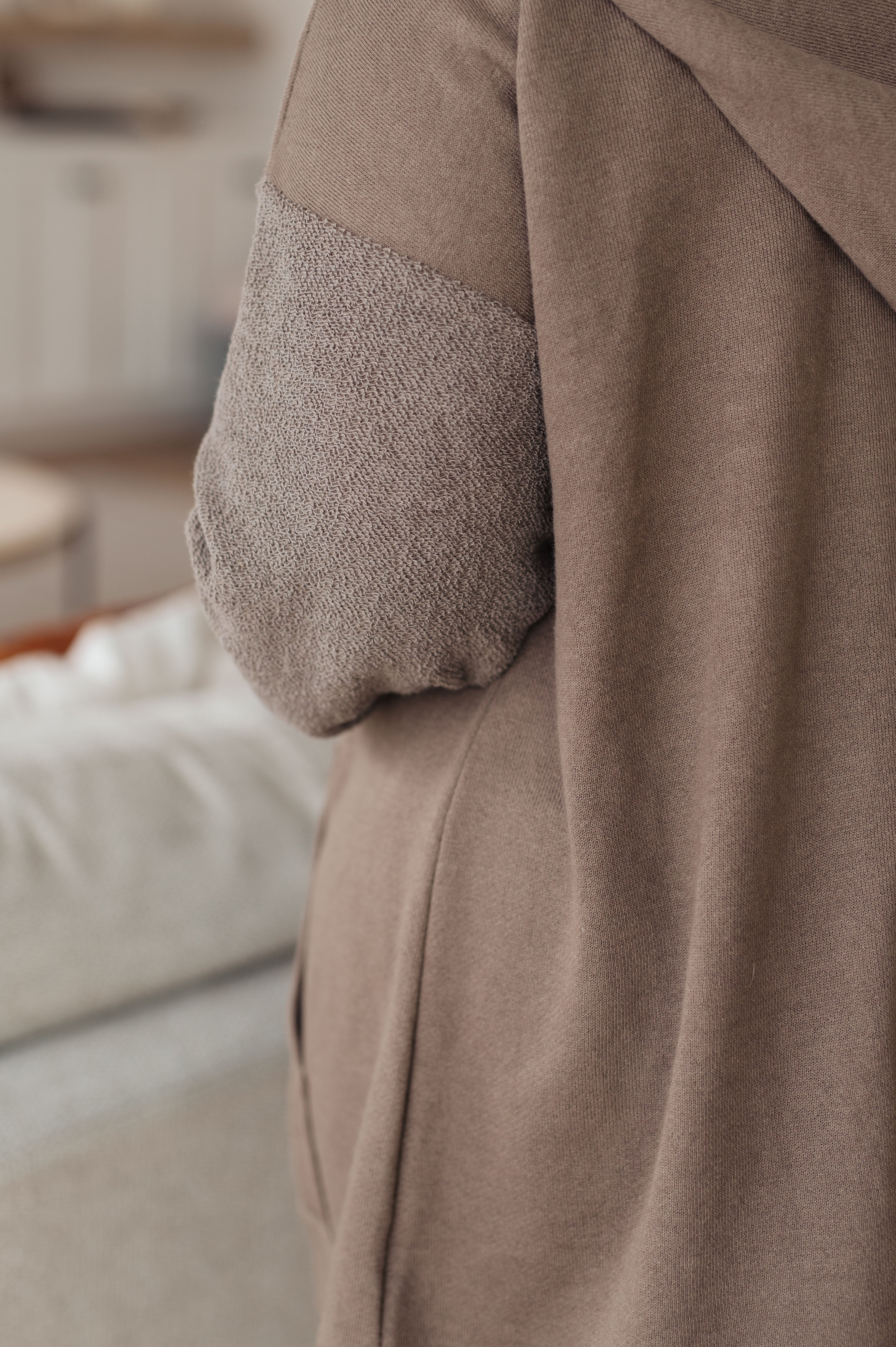 Close-up of a brown zip up hoodie with textured elbow area against a blurred background.