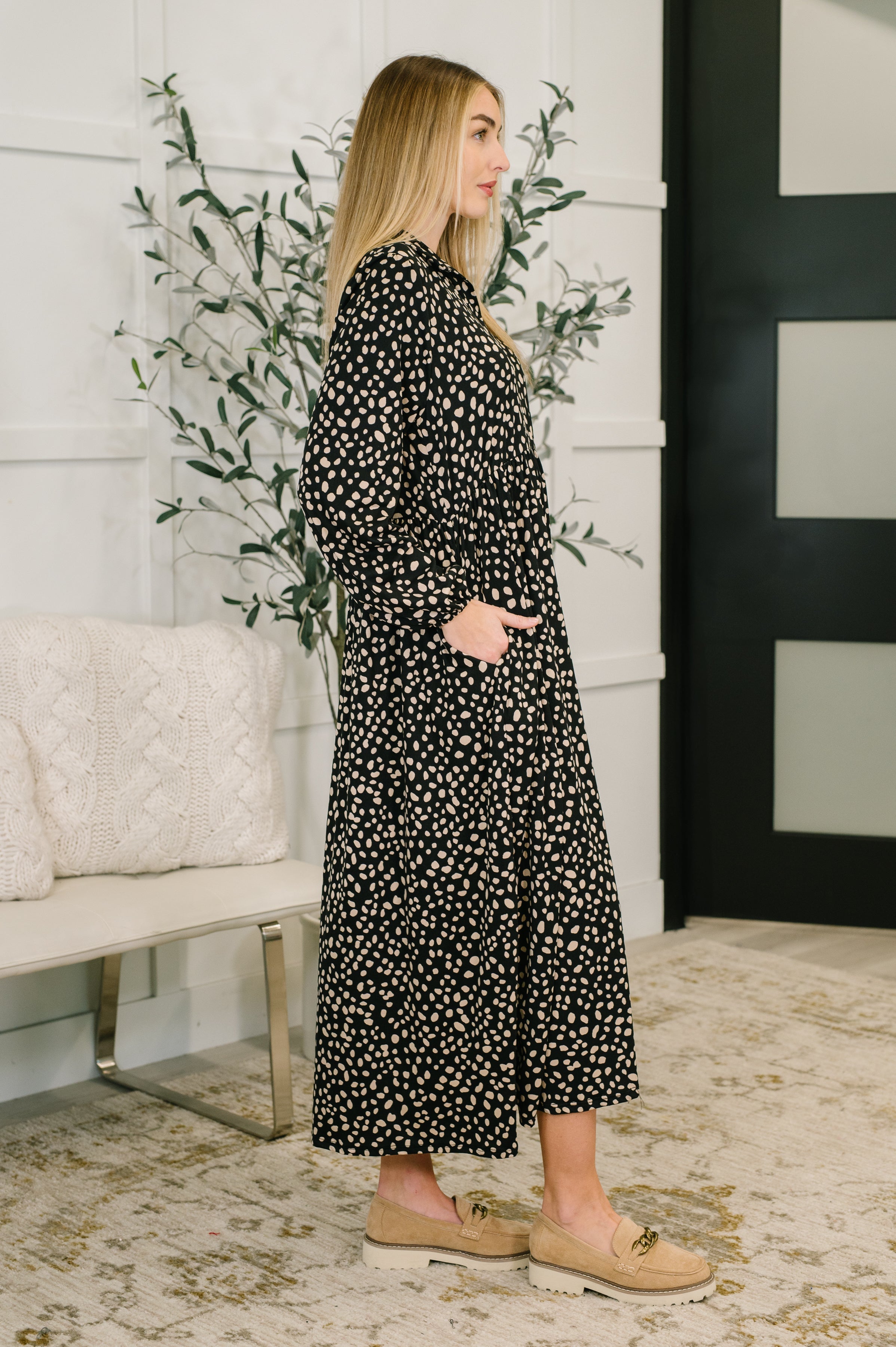 Woman wearing a black collared maxi dress with brown spots and tan shoes in an indoor setting.