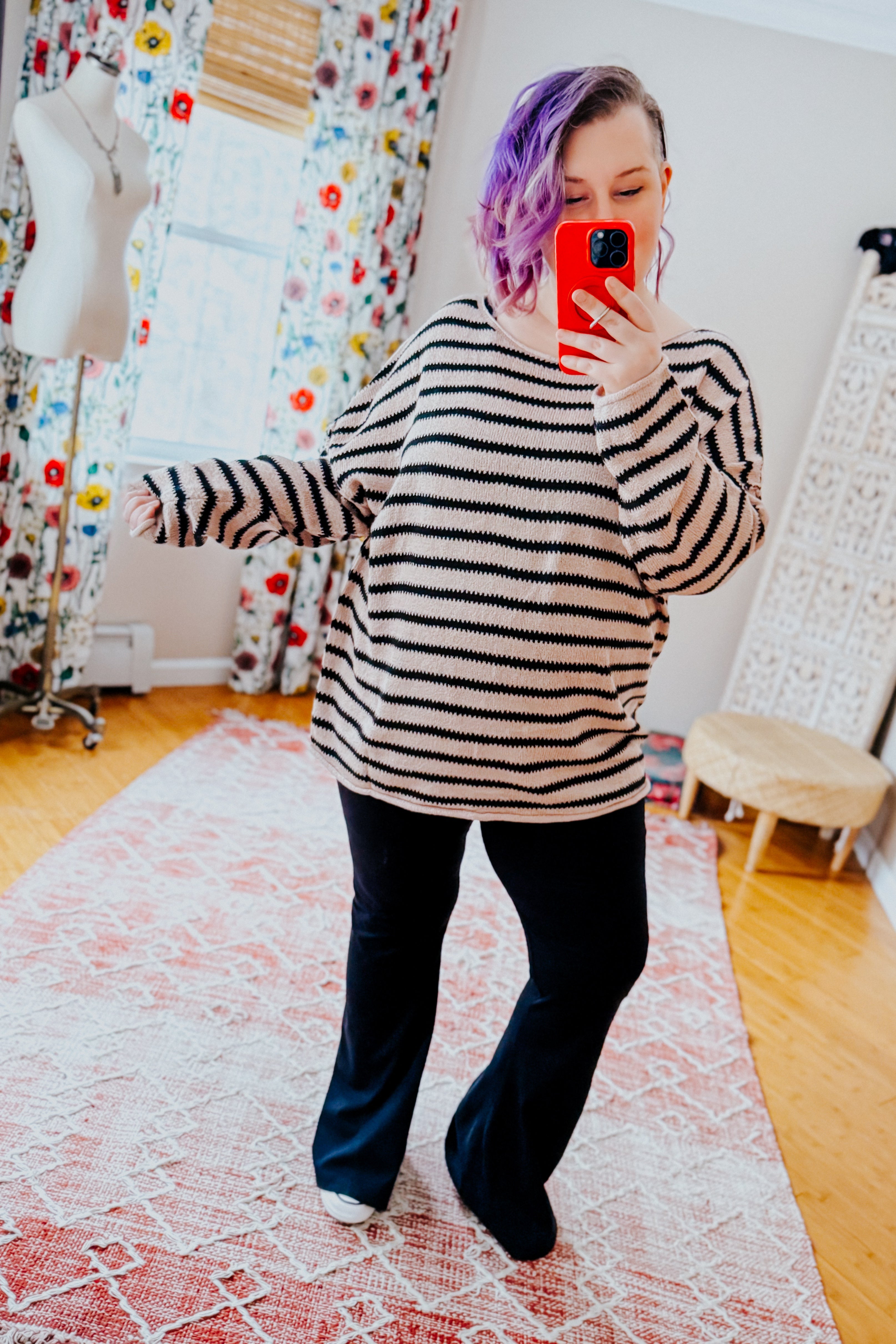 Woman wearing a taupe long sleeve sweater with black stripes and yoga pants in an indoor setting.