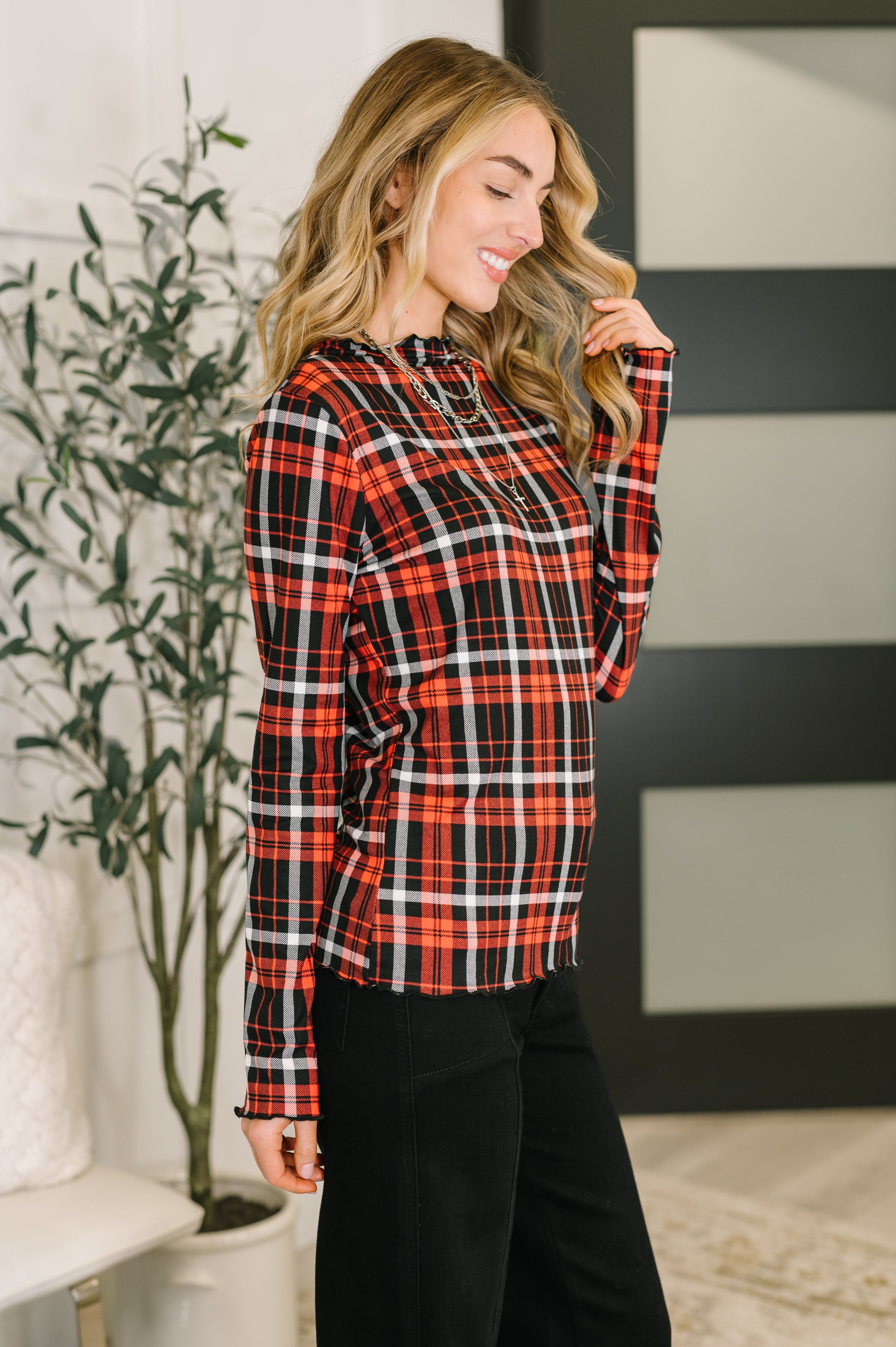 Woman wearing a red and black sheer plaid shirt and black jeans in an indoor setting
