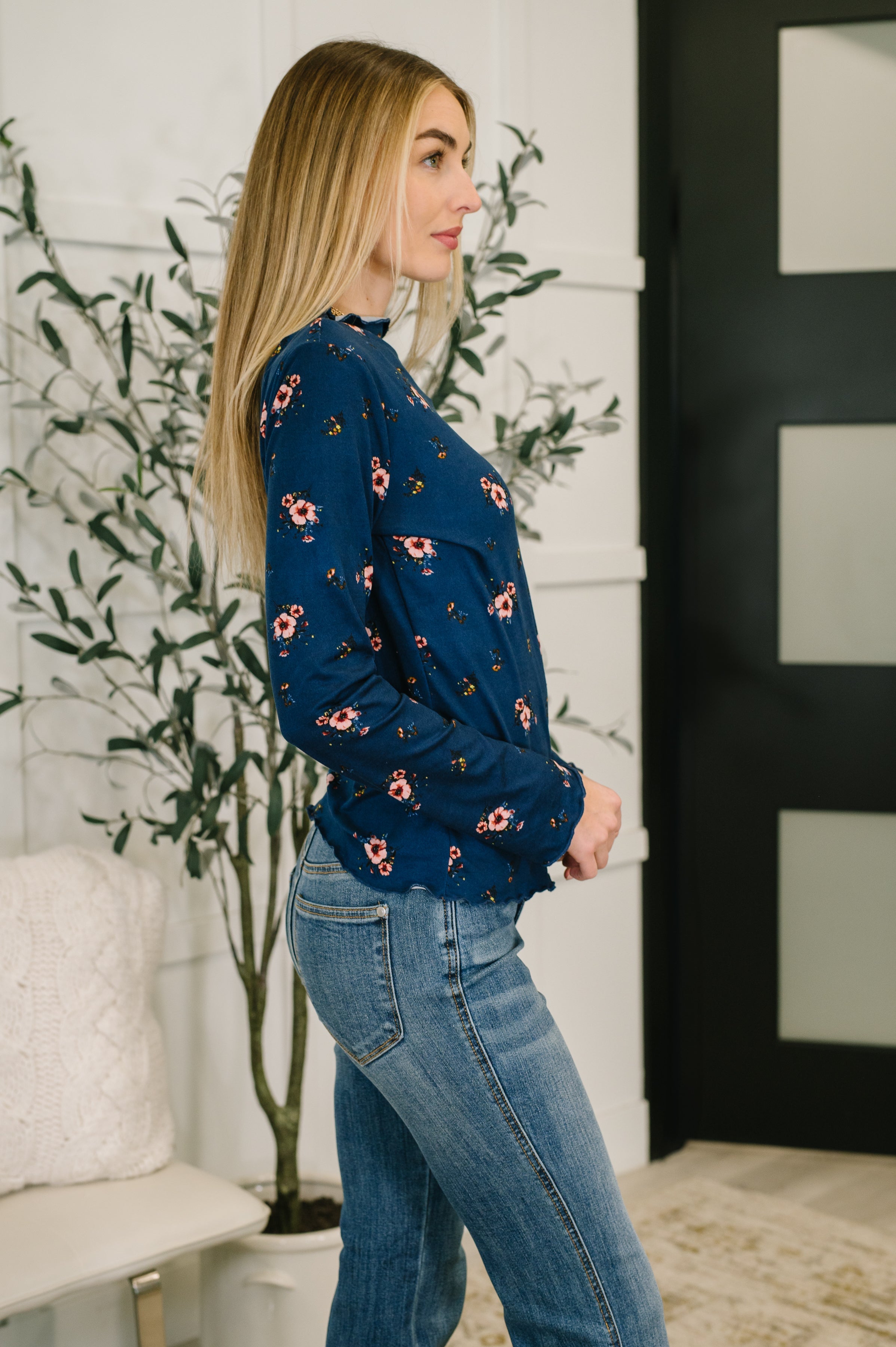 Woman wearing a blue floral top and blue jeans standing indoors.