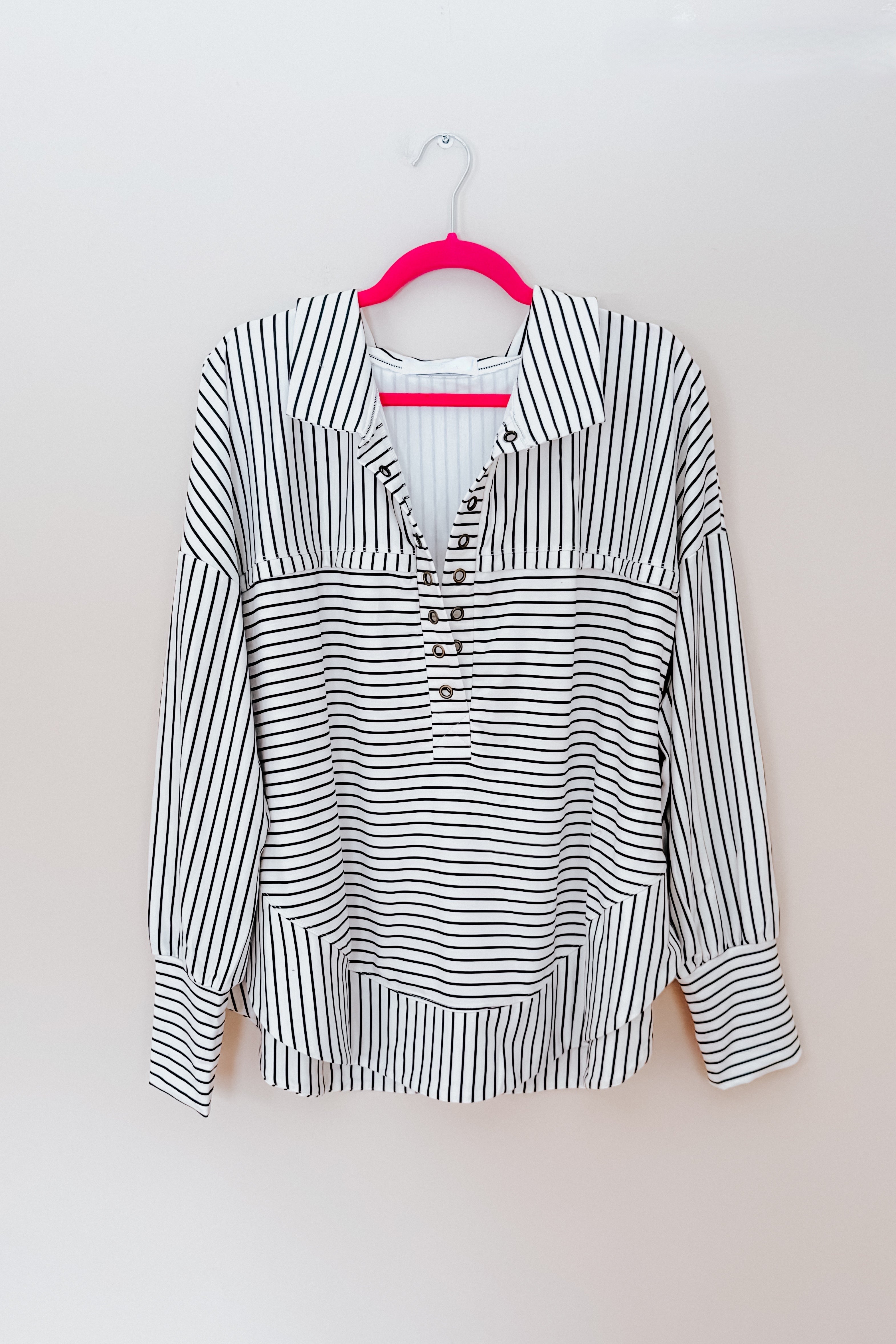 A white and black striped collared pullover top hanging from a bright pink hanger.