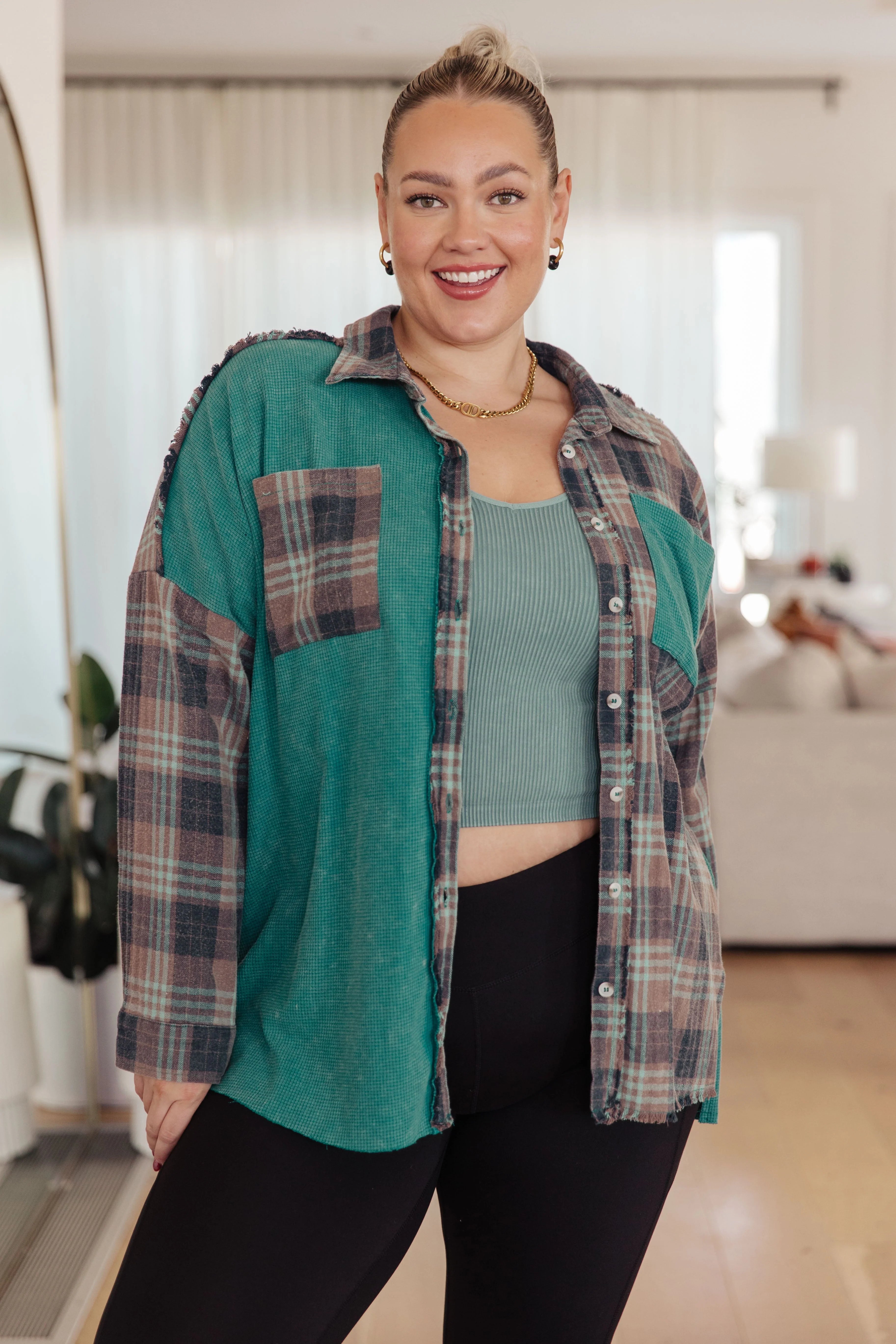 Woman wearing a teal plaid button up shirt over a teal tank top and black leggings in an indoor setting.