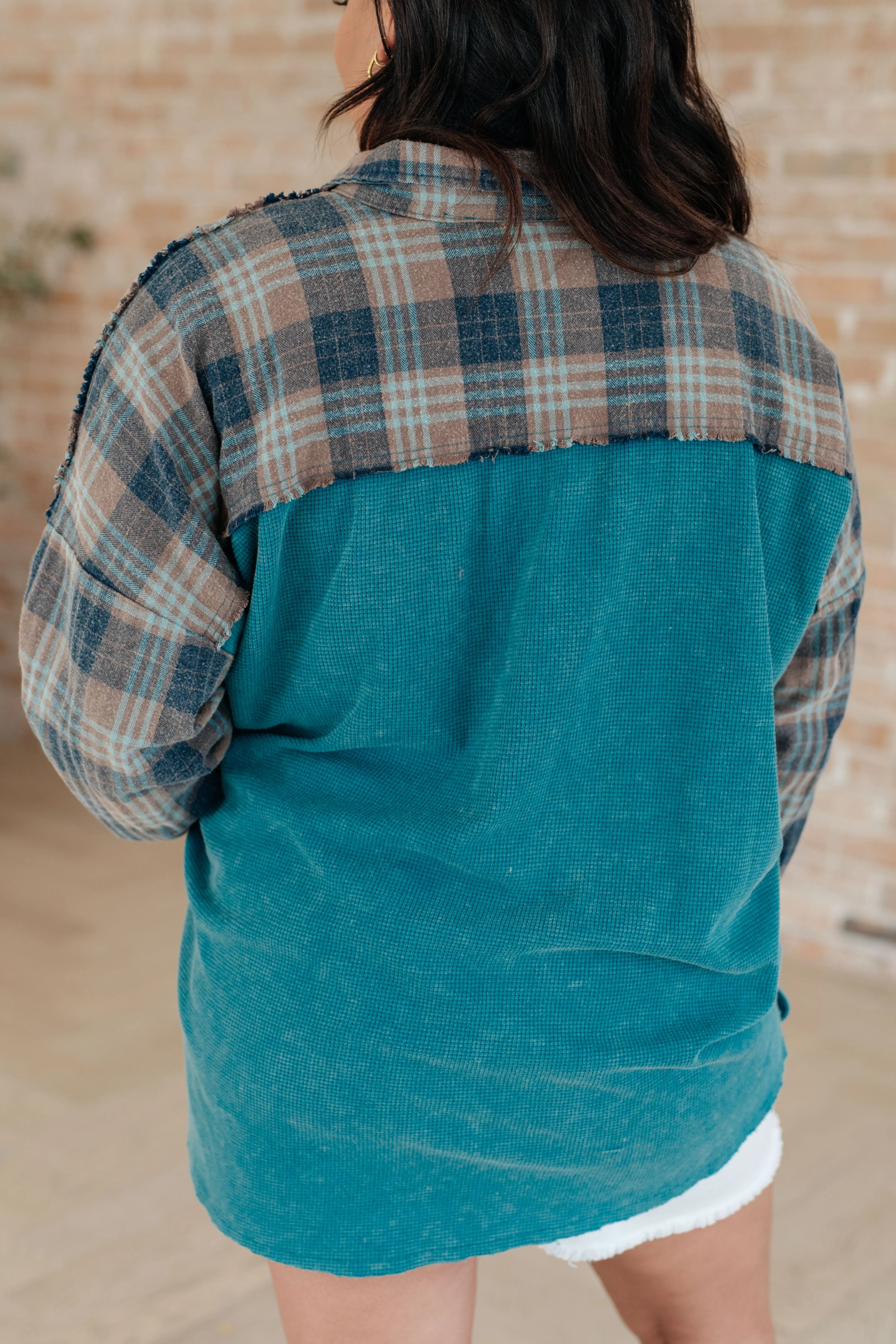 Woman with her back facing the camera wearing a blue plaid shirt with a beige background