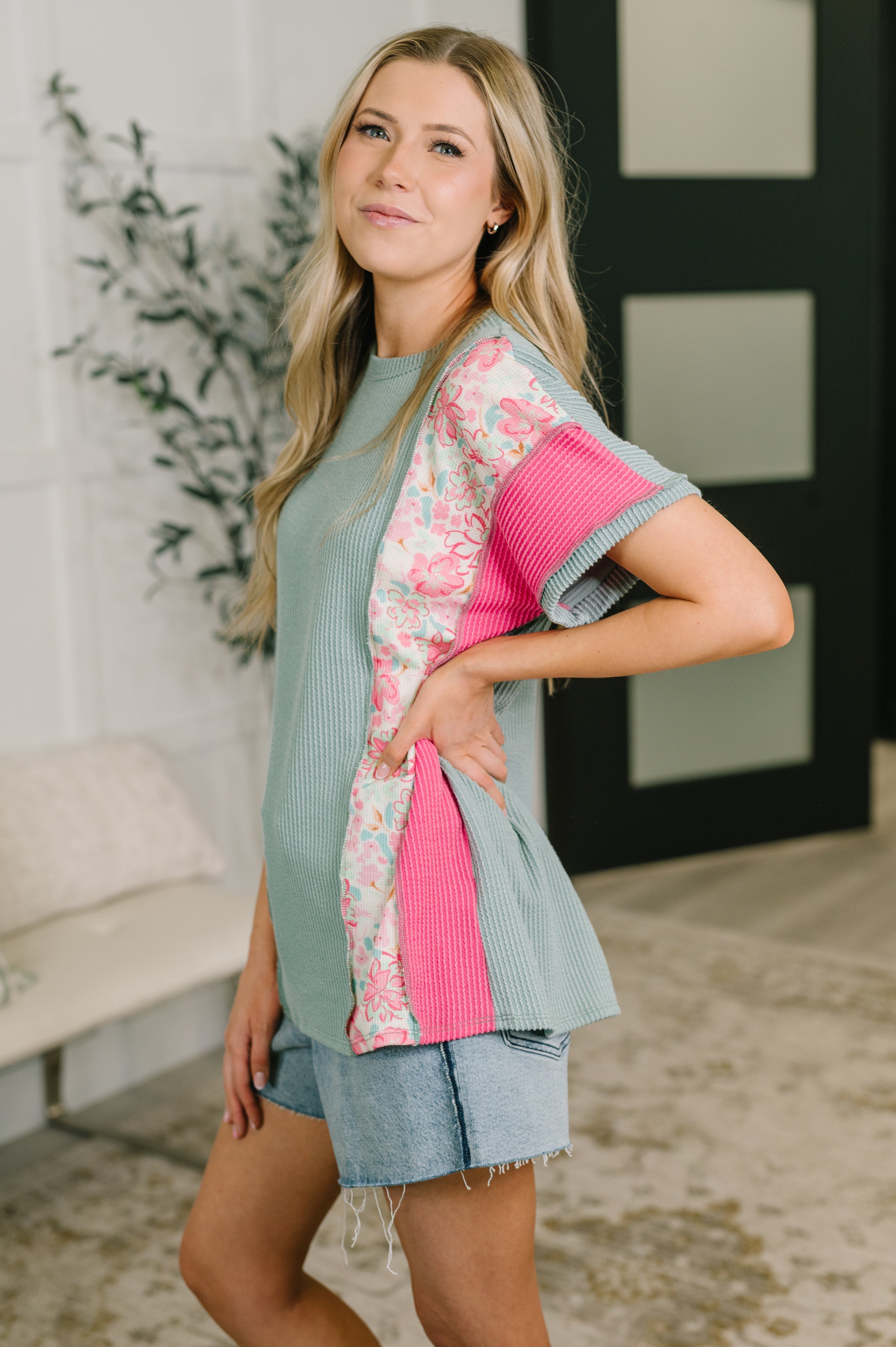 Woman wearing cozy knit top with blue, pink panels and floral detail paired with denim shorts indoors