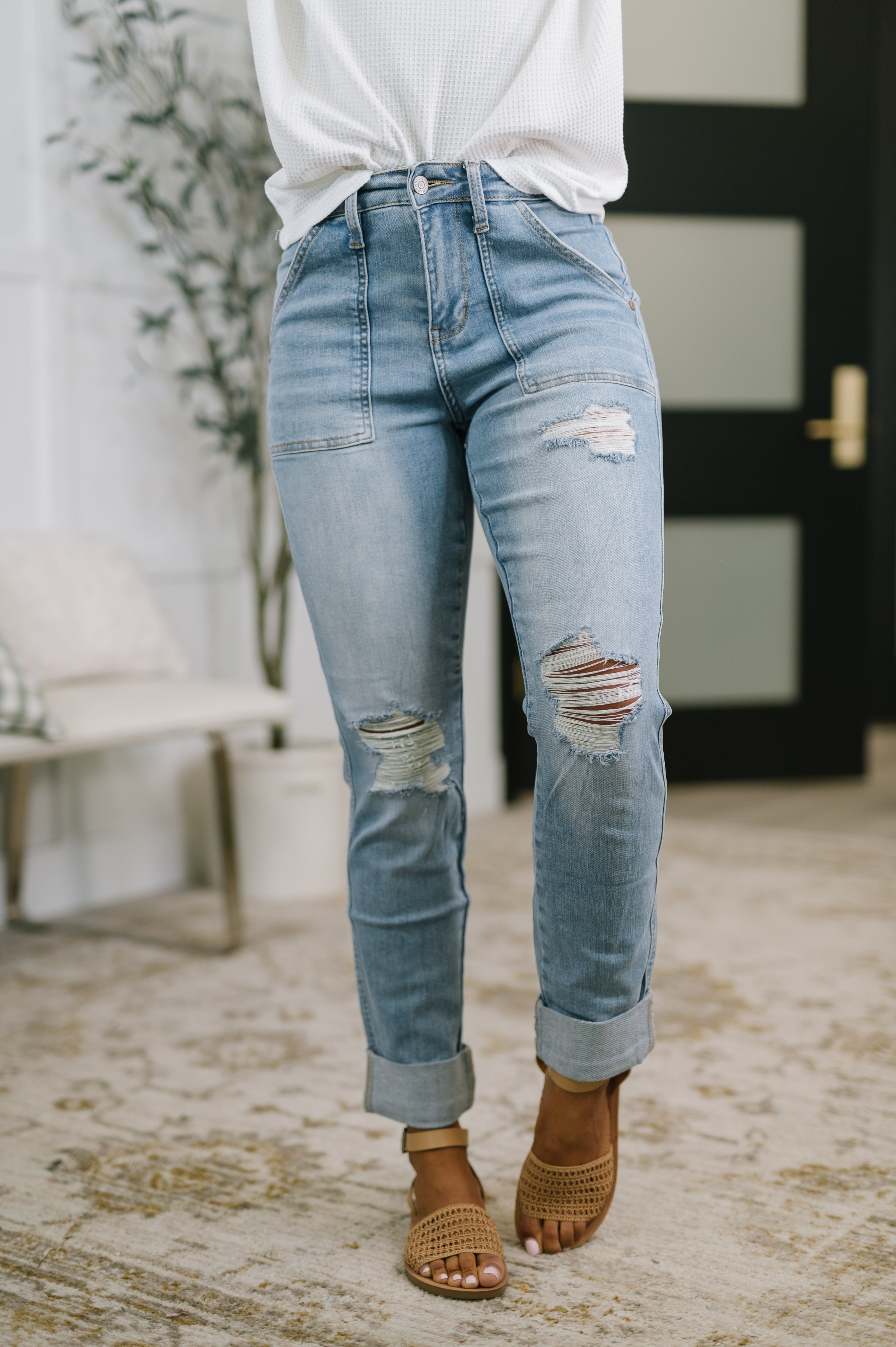 Woman wearing light blue high-rise distressed jeans with cuffed hems and tan woven sandals indoors