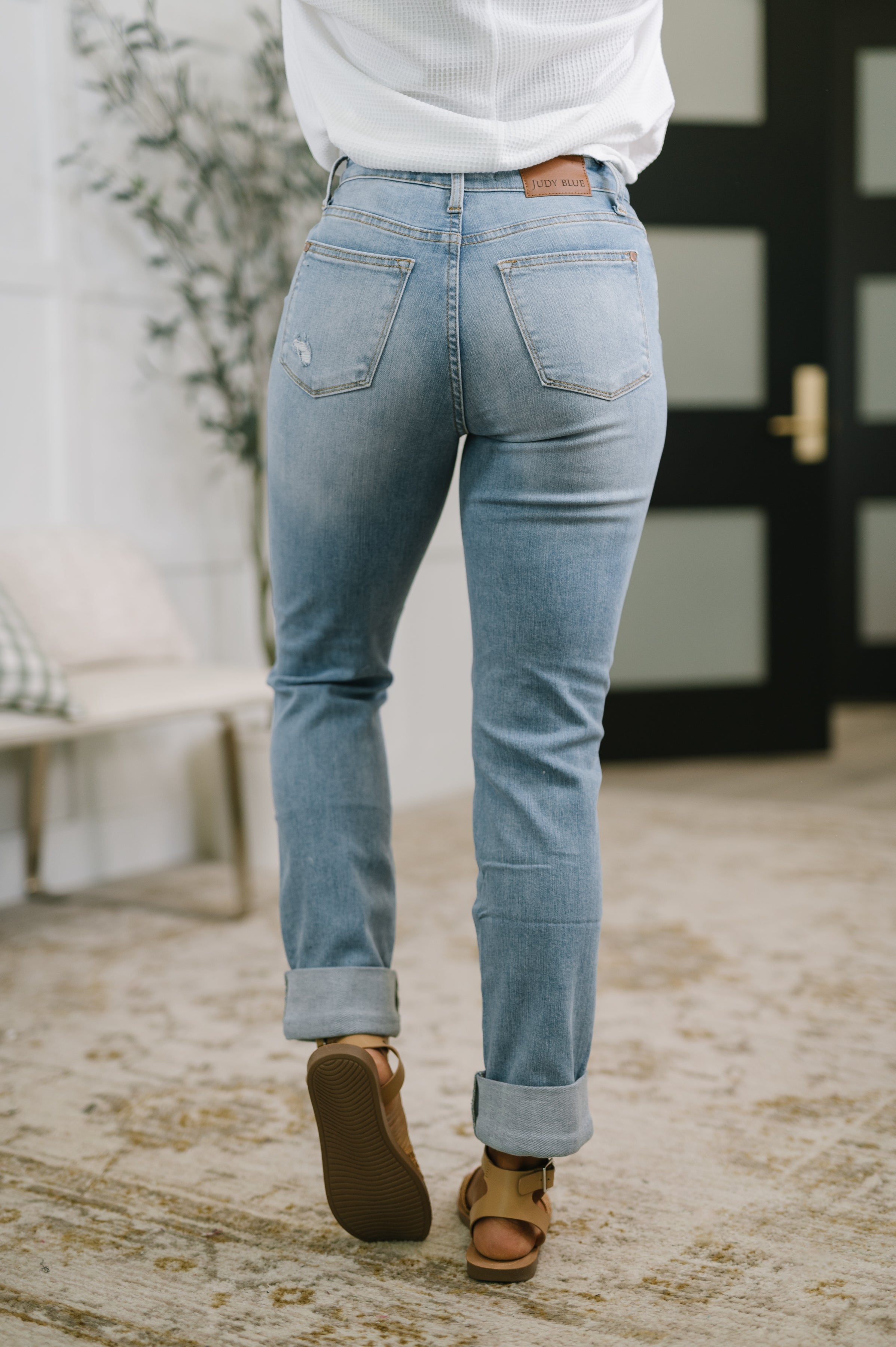 Woman wearing light blue distressed high-rise jeans with cuffed hems and tan sandals in cozy indoor space