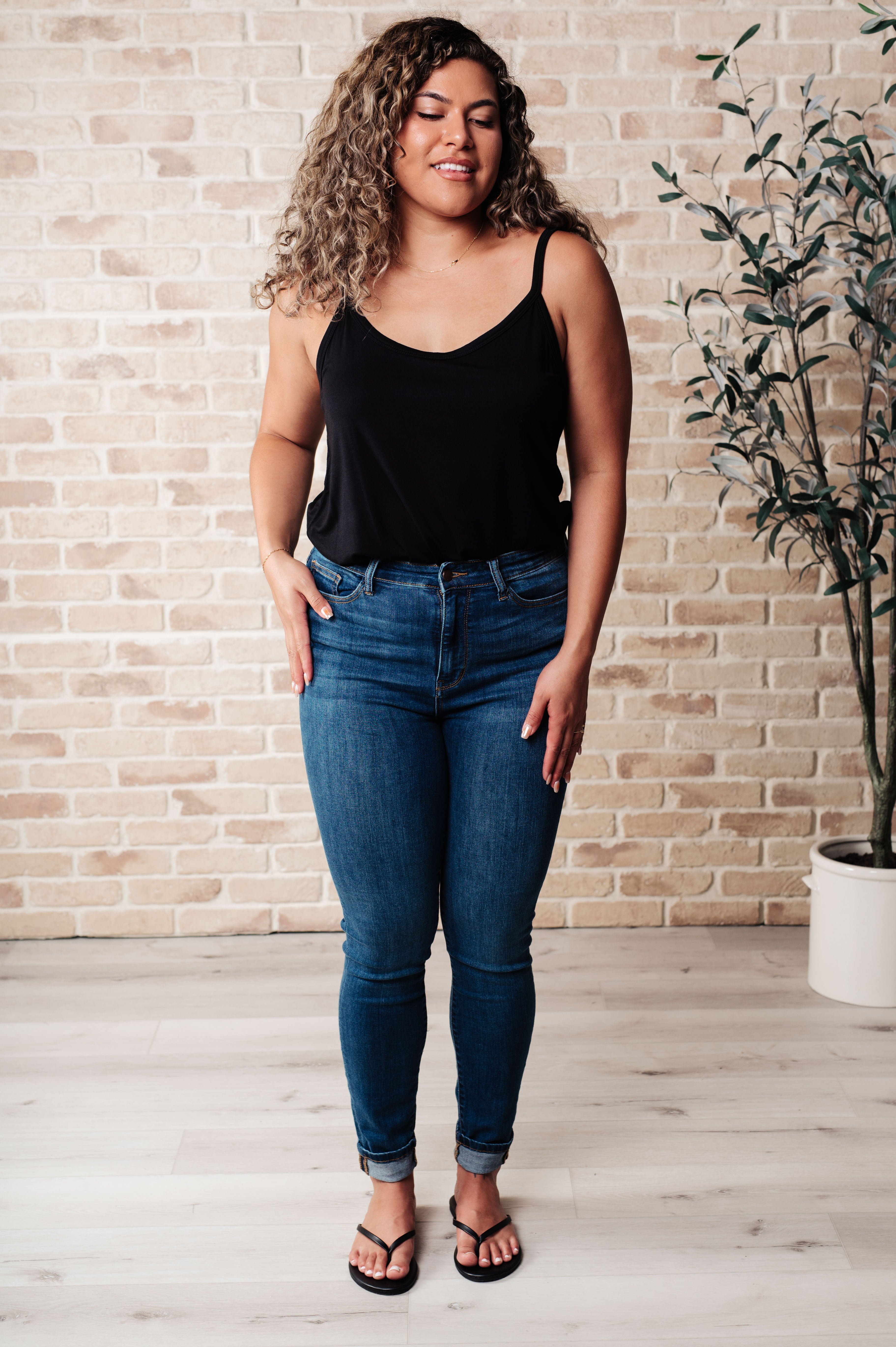 Full front view of woman wearing black Ain't No Mountain High Enough tank with thin straps and dark blue skinny jeans indoors