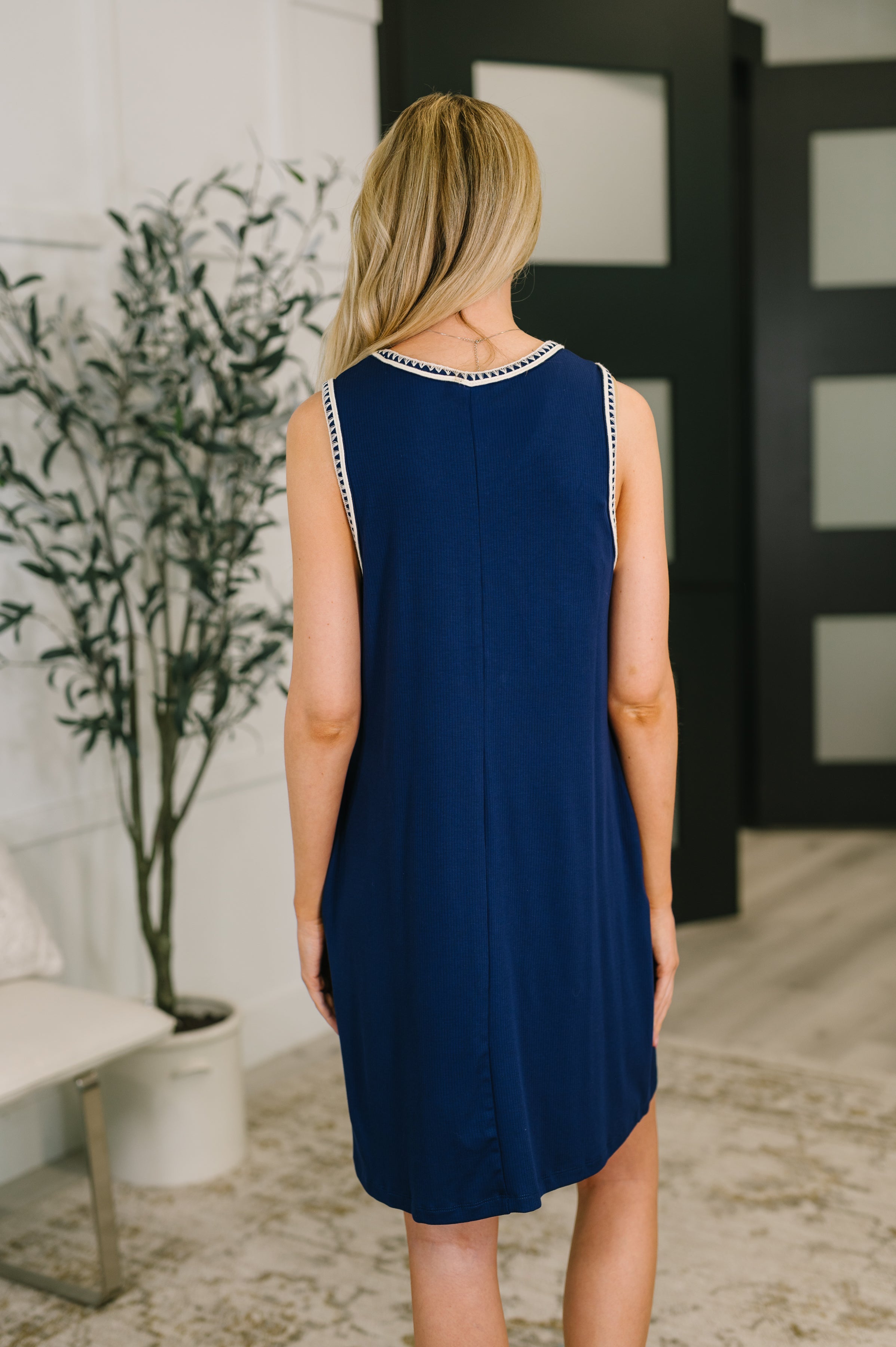 Woman wearing navy mini tank dress with trim detail shown from the back in relaxed indoor setting