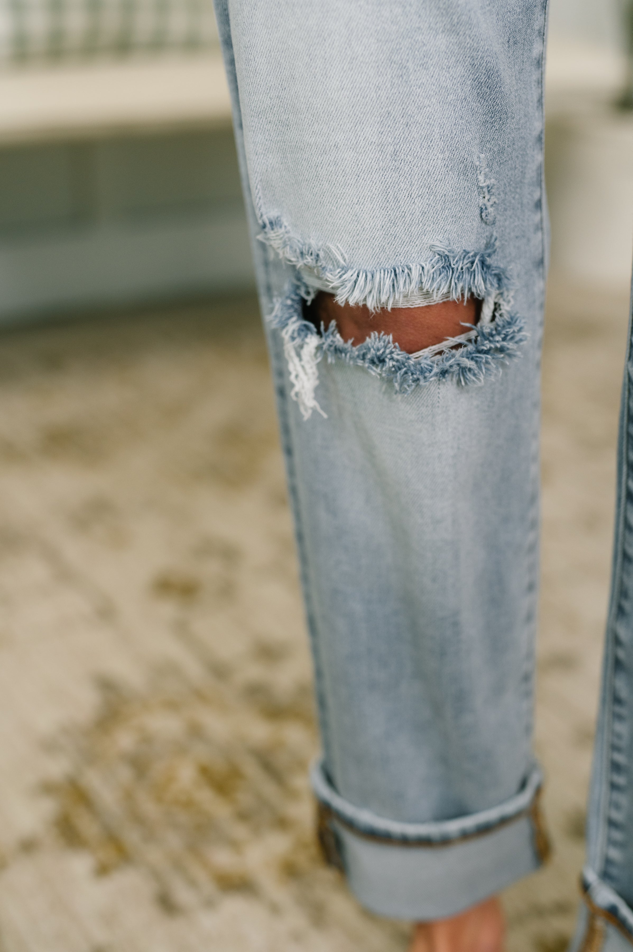 Close-up of light blue distressed boyfriend jeans with rolled cuffs showing skin through a ripped knee detail.