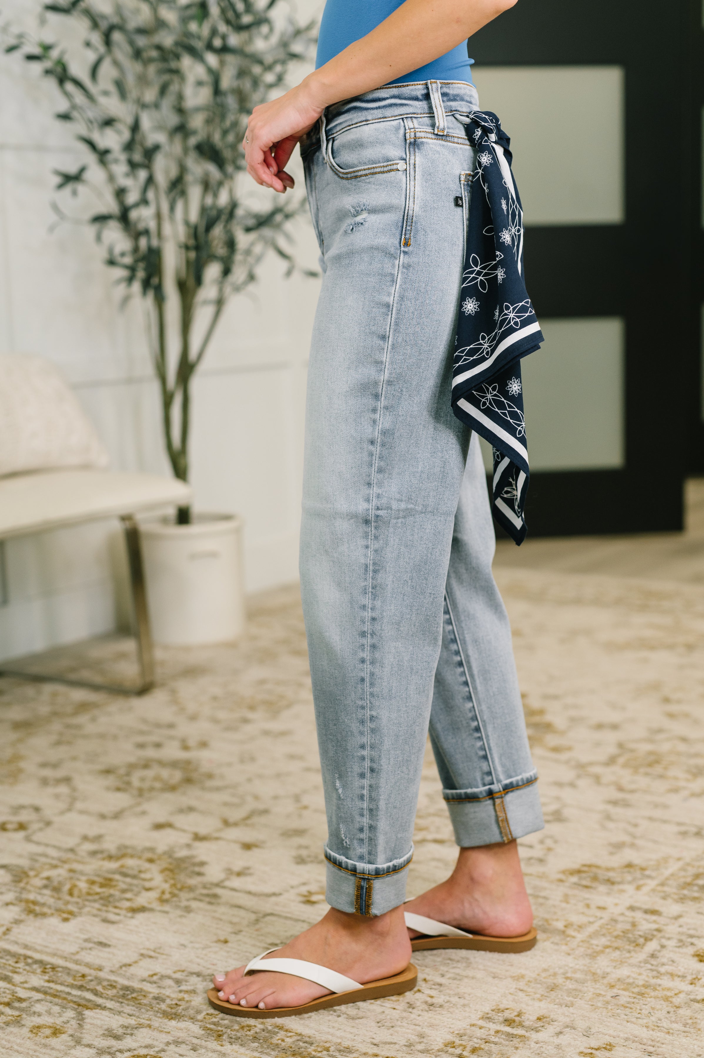 Side view of light wash mid-rise boyfriend jeans with navy bandana loop and white sandals indoors
