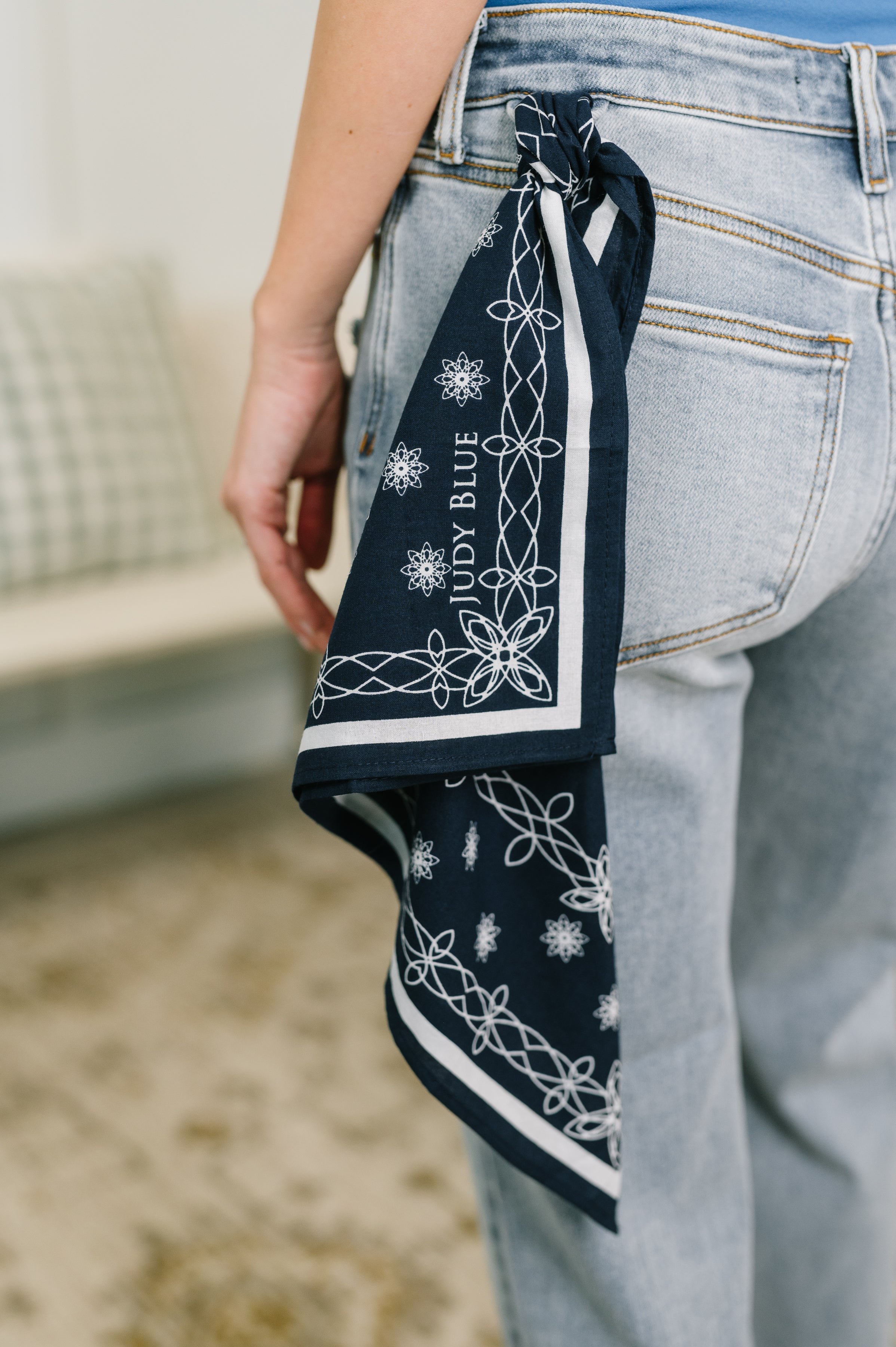 Close-up of light wash mid-rise boyfriend jeans with a navy patterned bandana looped through the belt loop indoors