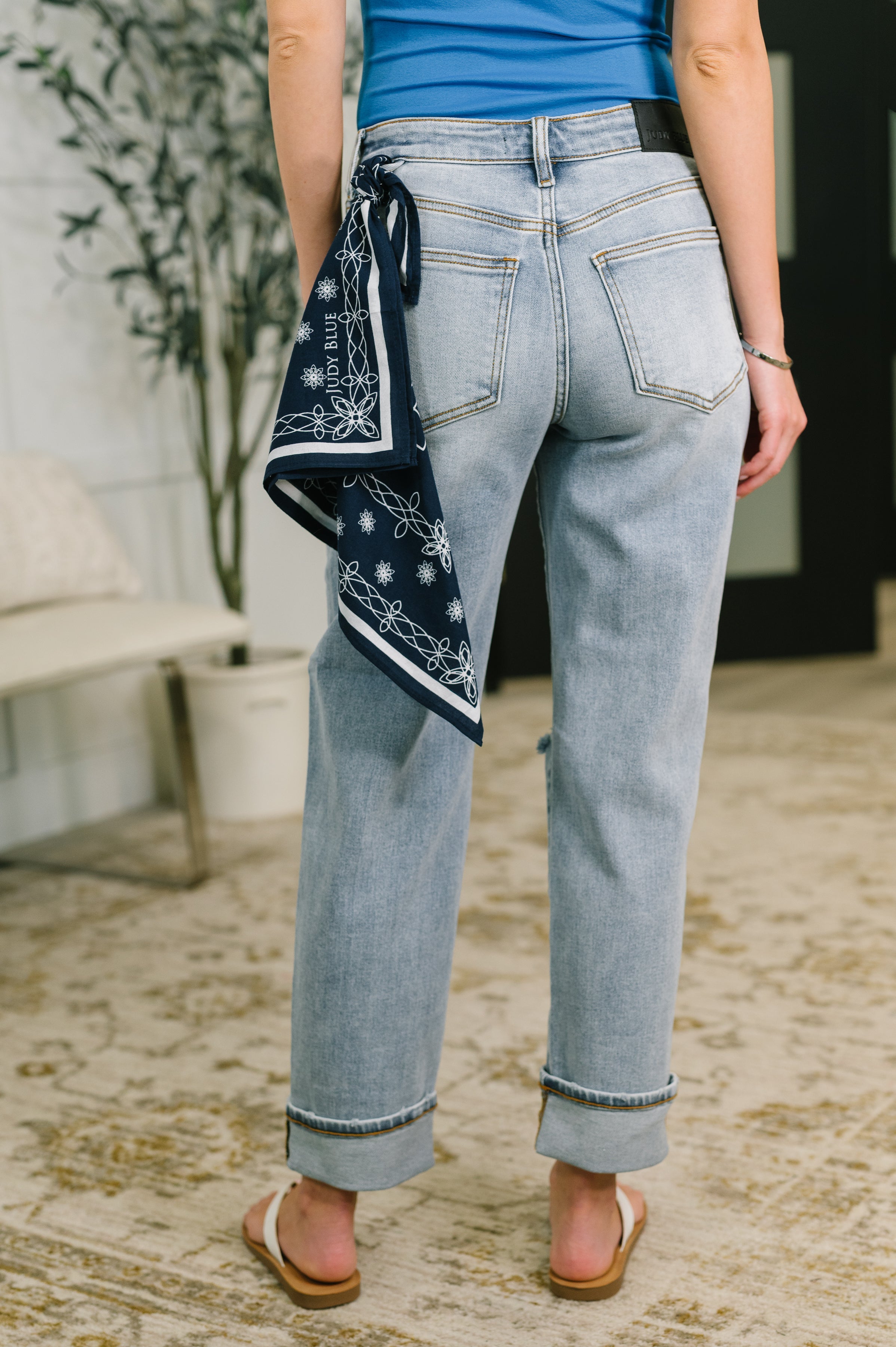 Back view of person wearing light blue mid rise boyfriend jeans with navy bandana loop and sandals indoors