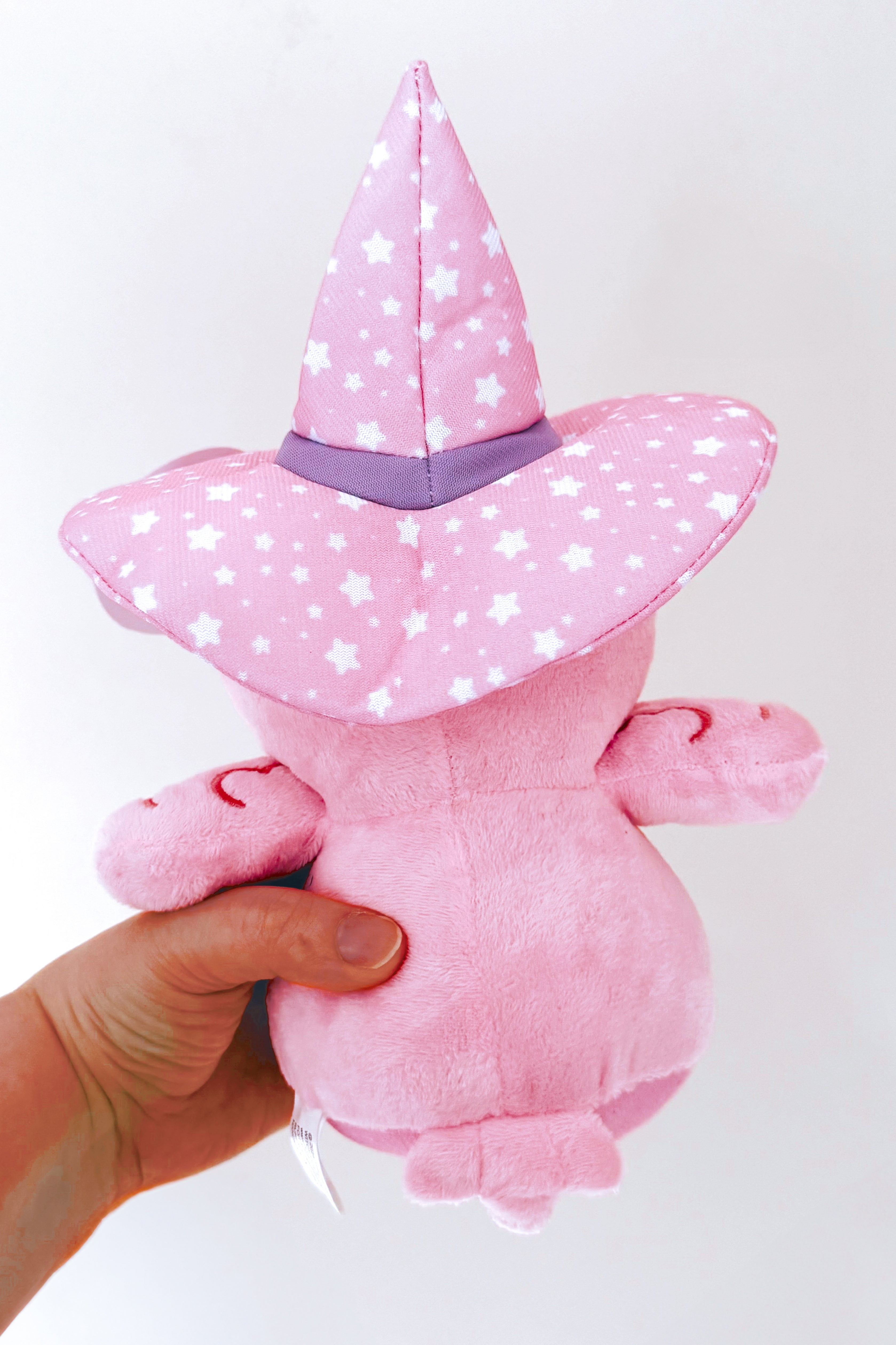 Hand holding Alice Crowley pink plush crow wearing a starry purple witch hat viewed from the back