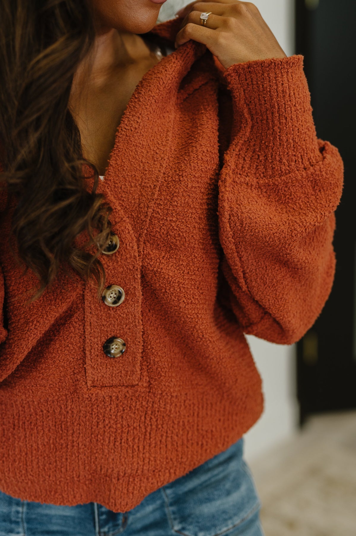 Close view of a woman wearing a rust textured knit sweater with V neckline half button front and blue jeans