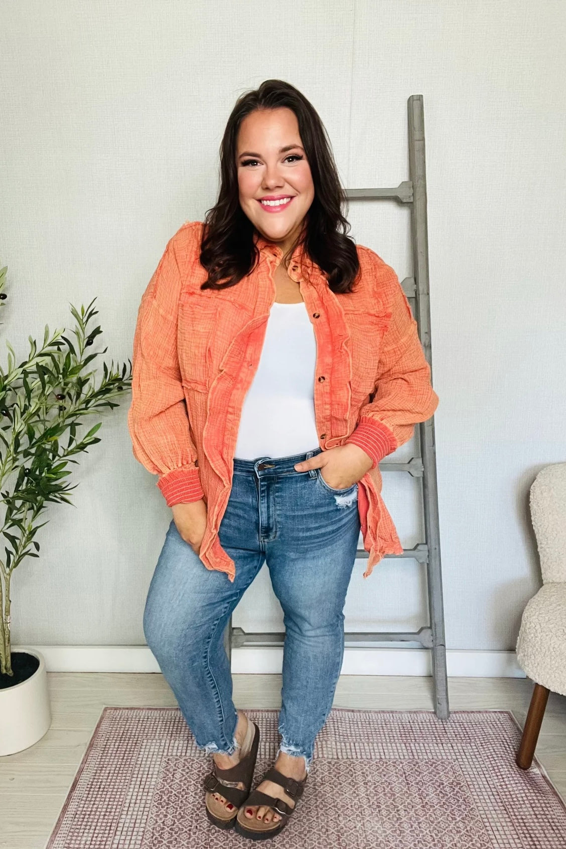 Smiling woman wearing orange textured All Pan Out Ruffled Button Up Shirt with puffed sleeves and blue jeans indoors