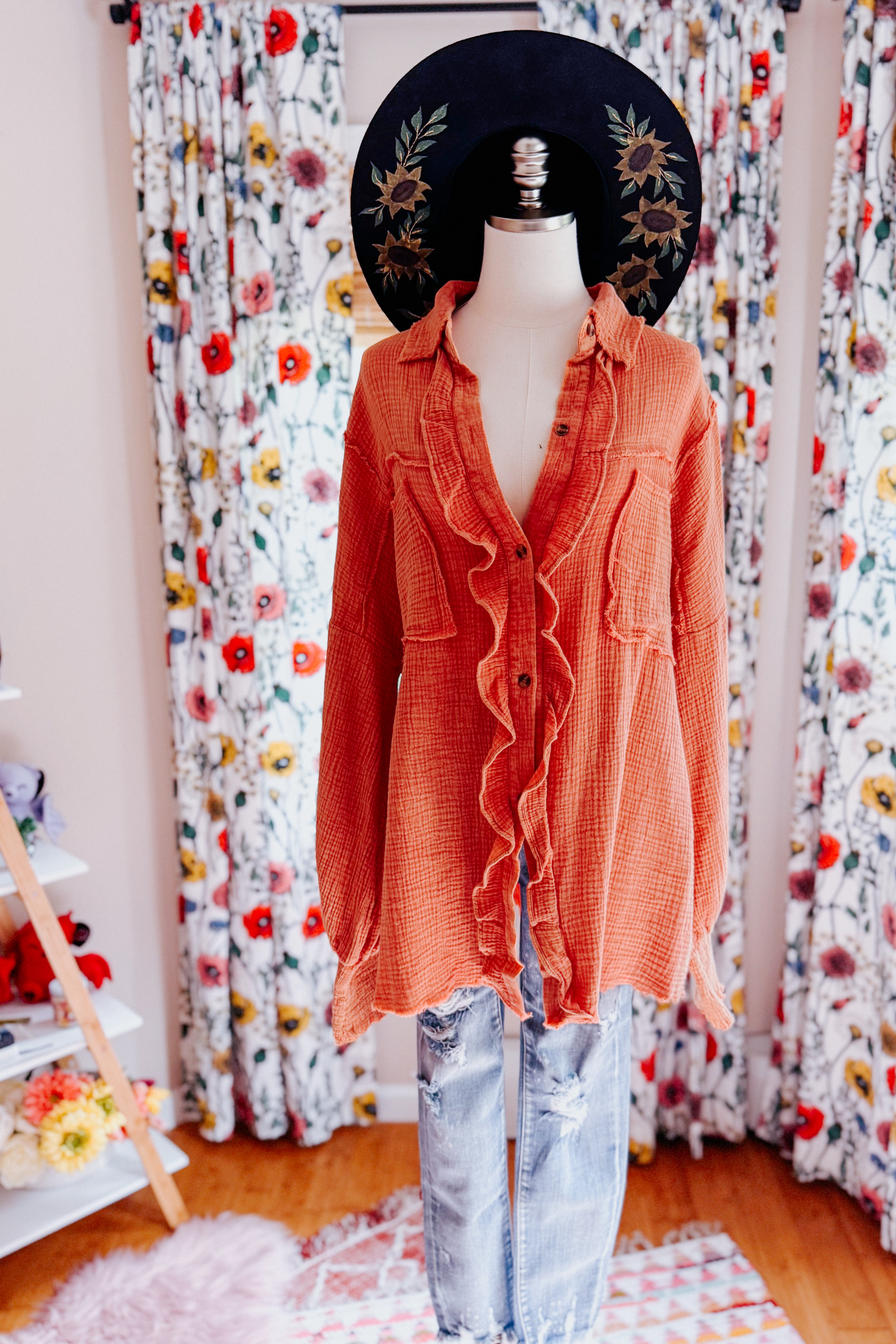 Orange All Pan Out Ruffled Button Up Shirt displayed on mannequin with floral hat and distressed jeans in home setting
