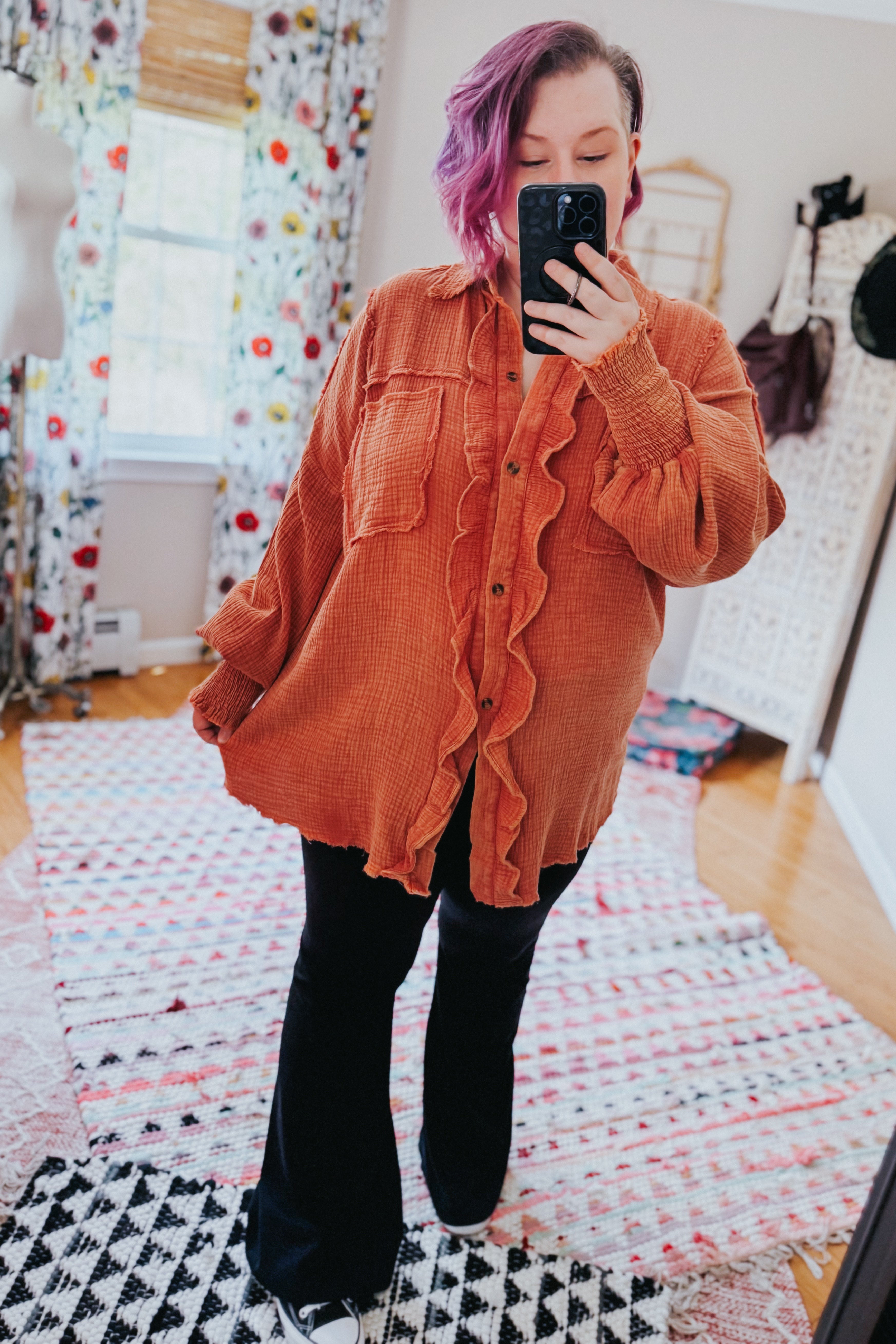 Woman with purple hair taking mirror selfie wearing oversized orange All Pan Out Ruffled Button Up Shirt with textured fabric in bedroom