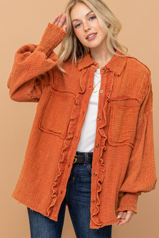 Blonde woman wearing oversized textured burnt orange ruffled button-up shirt with smocked cuffs front view at gallery start