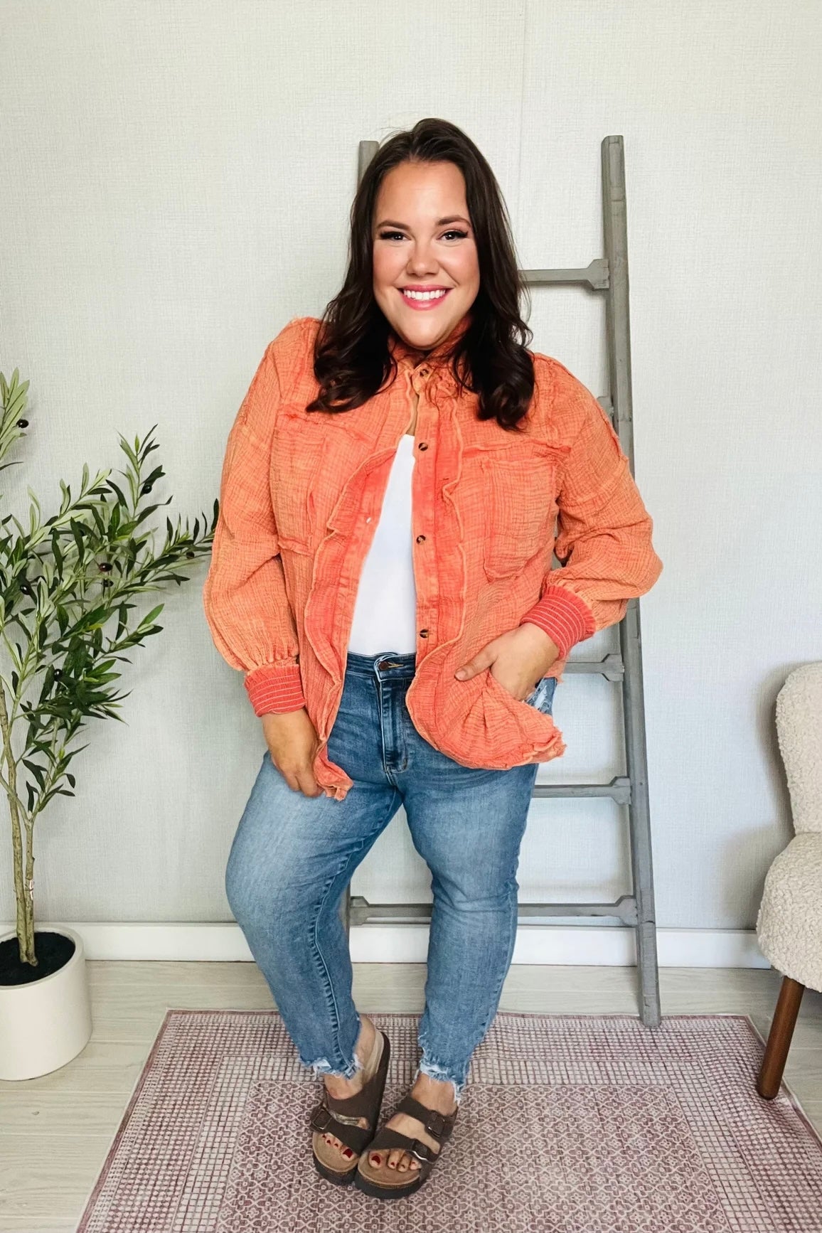 Smiling woman in orange All Pan Out Ruffled Button Up Shirt with puffed sleeves styled with light denim jeans indoors