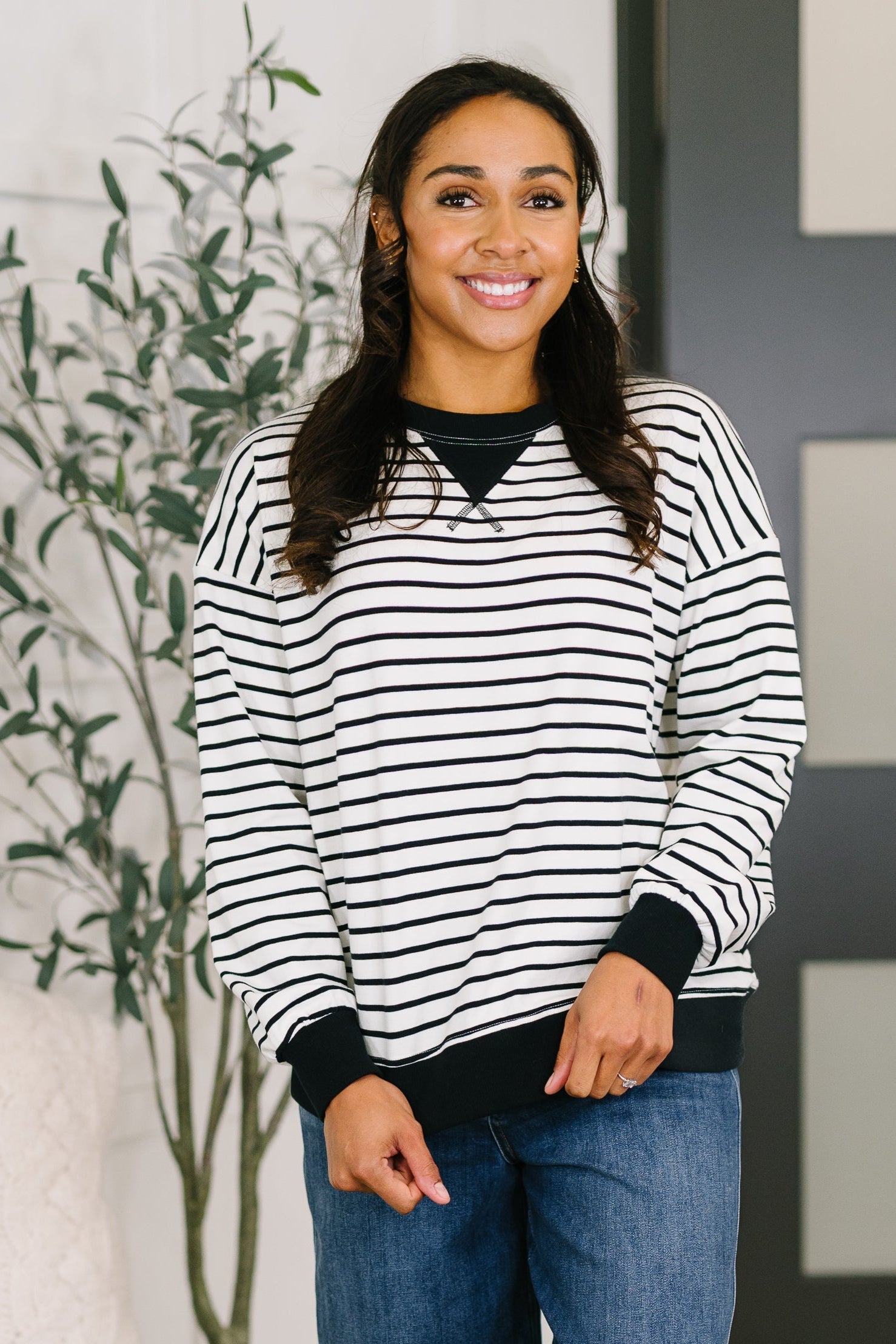 Smiling woman wearing black and white striped Almost Therapeutic Drop Shoulder Pullover with black cuffs and hem standing indoors