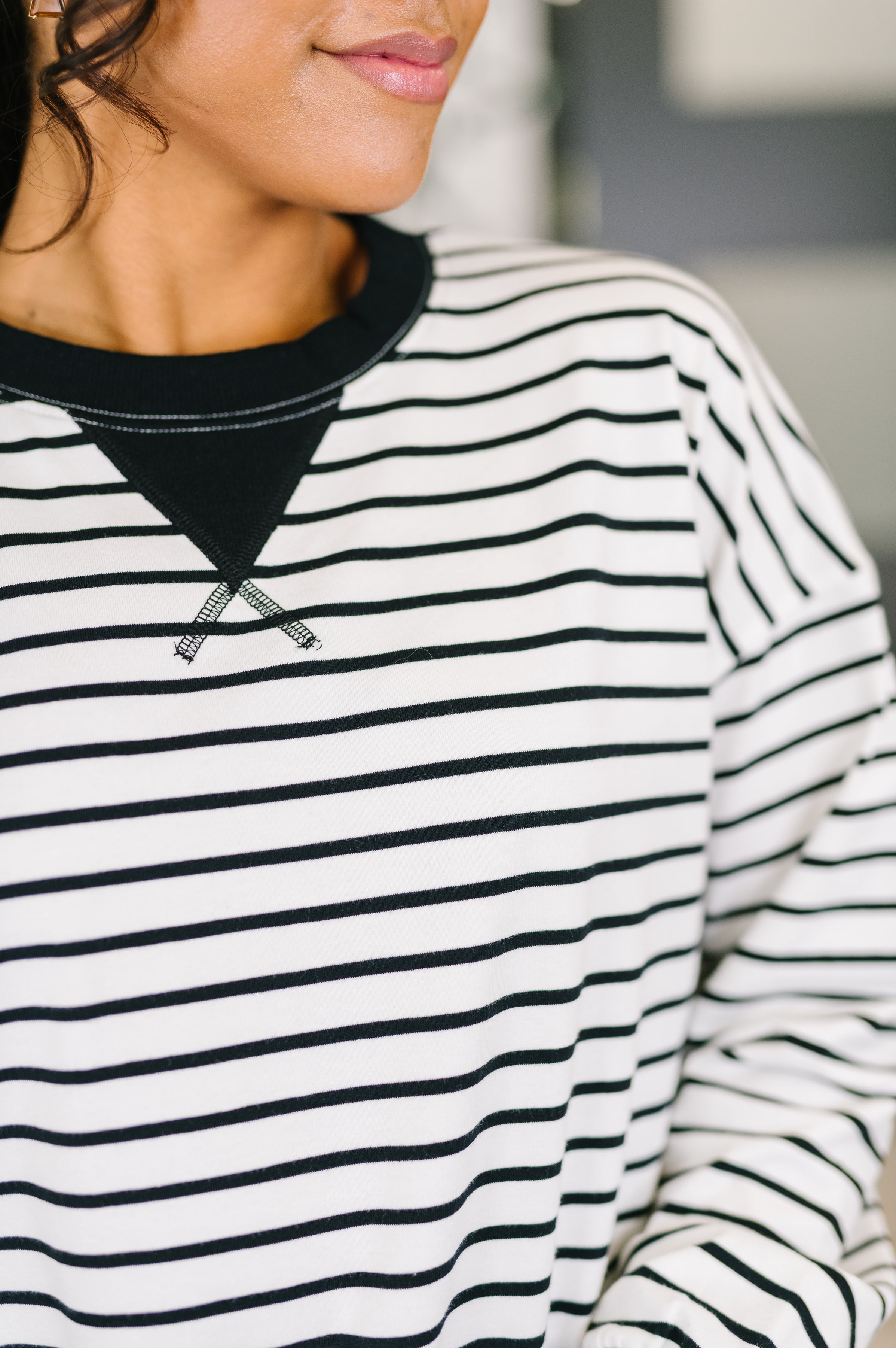 Close-up of black and white striped Almost Therapeutic Drop Shoulder Pullover collar and chest details on model indoors