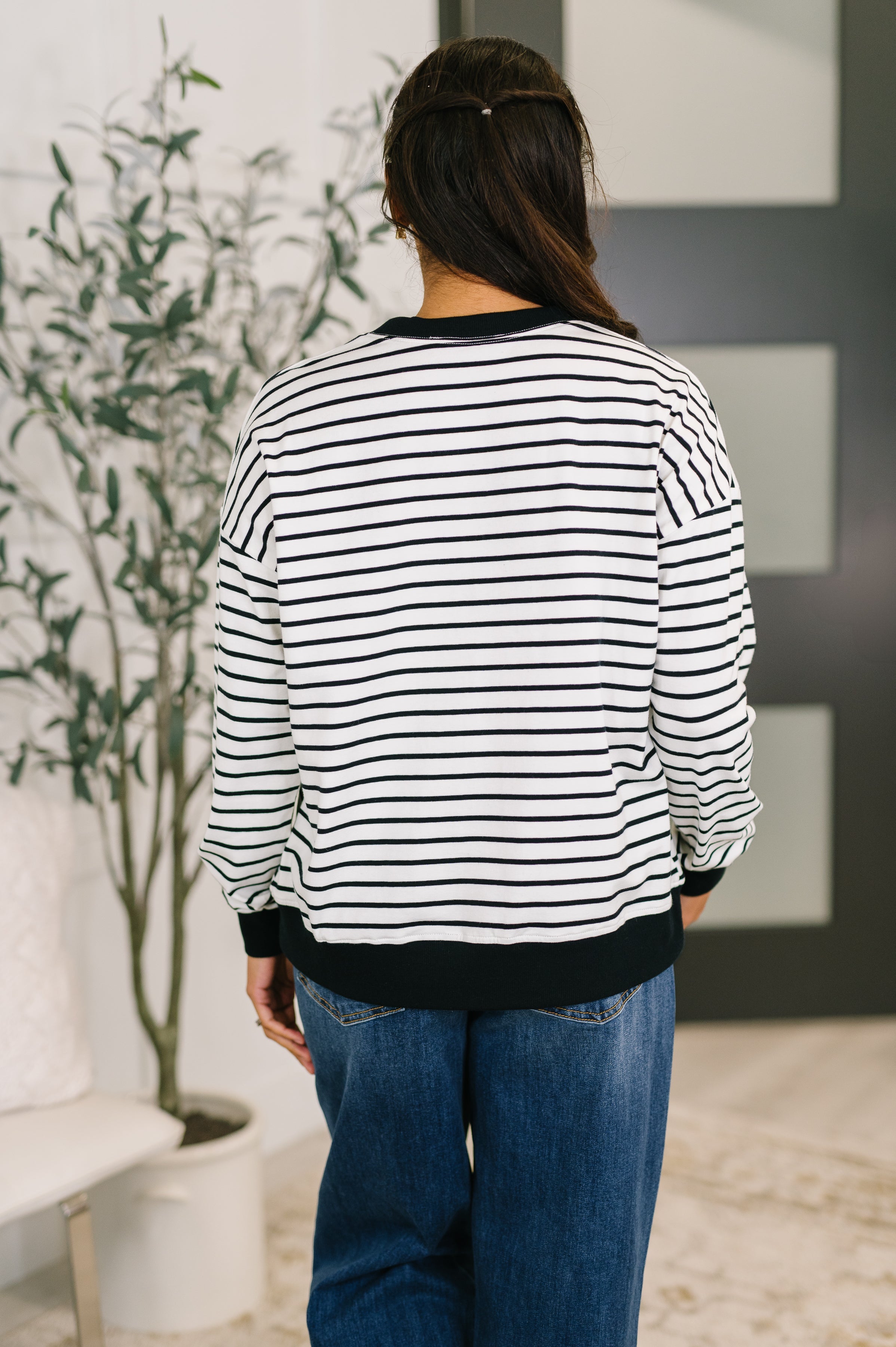Woman wearing black and white striped Almost Therapeutic Drop Shoulder Pullover standing indoors with back to camera