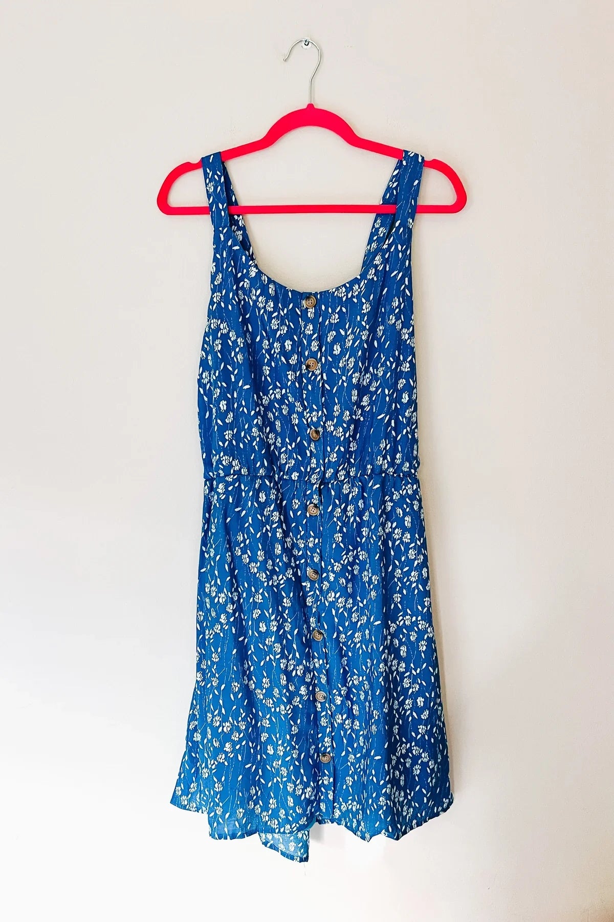 A blue summer floral dress hanging from a pink hanger.