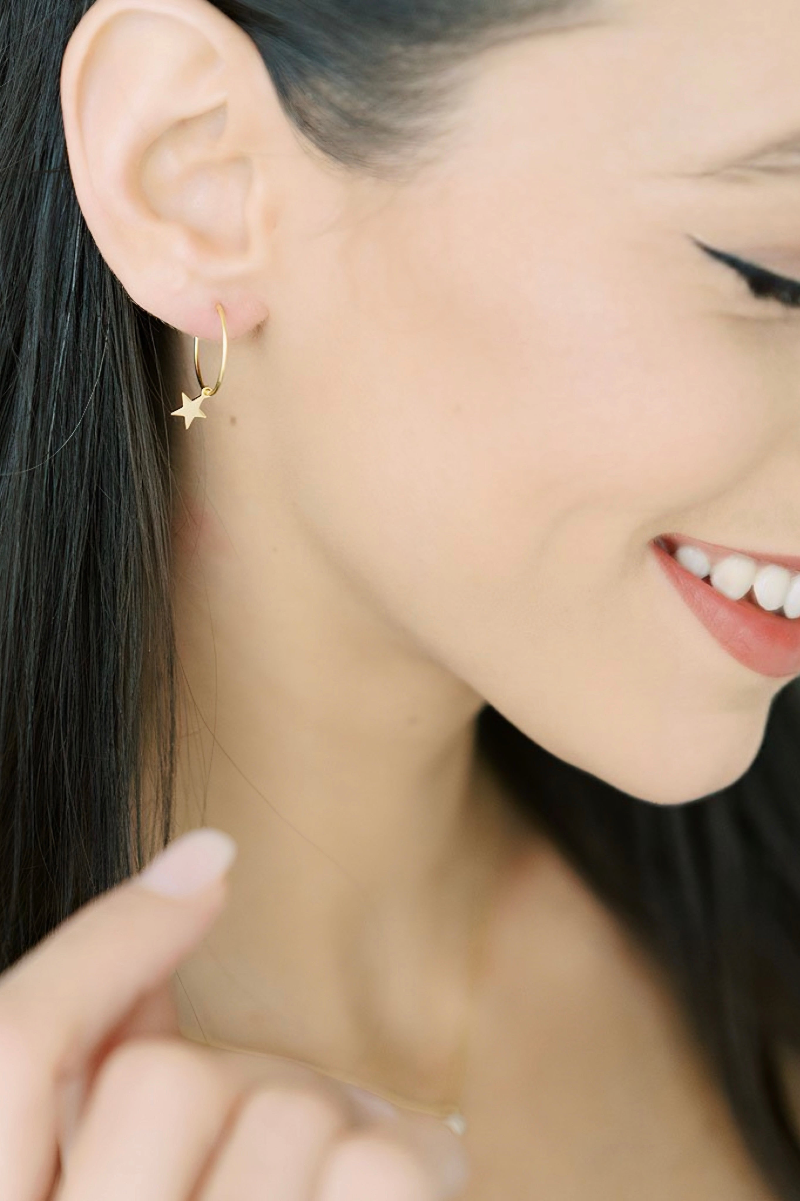 Close-up side view of a smiling woman wearing delicate gold star charm hoop earring AstraMagicCharmStarHoopEarrings2.jpg
