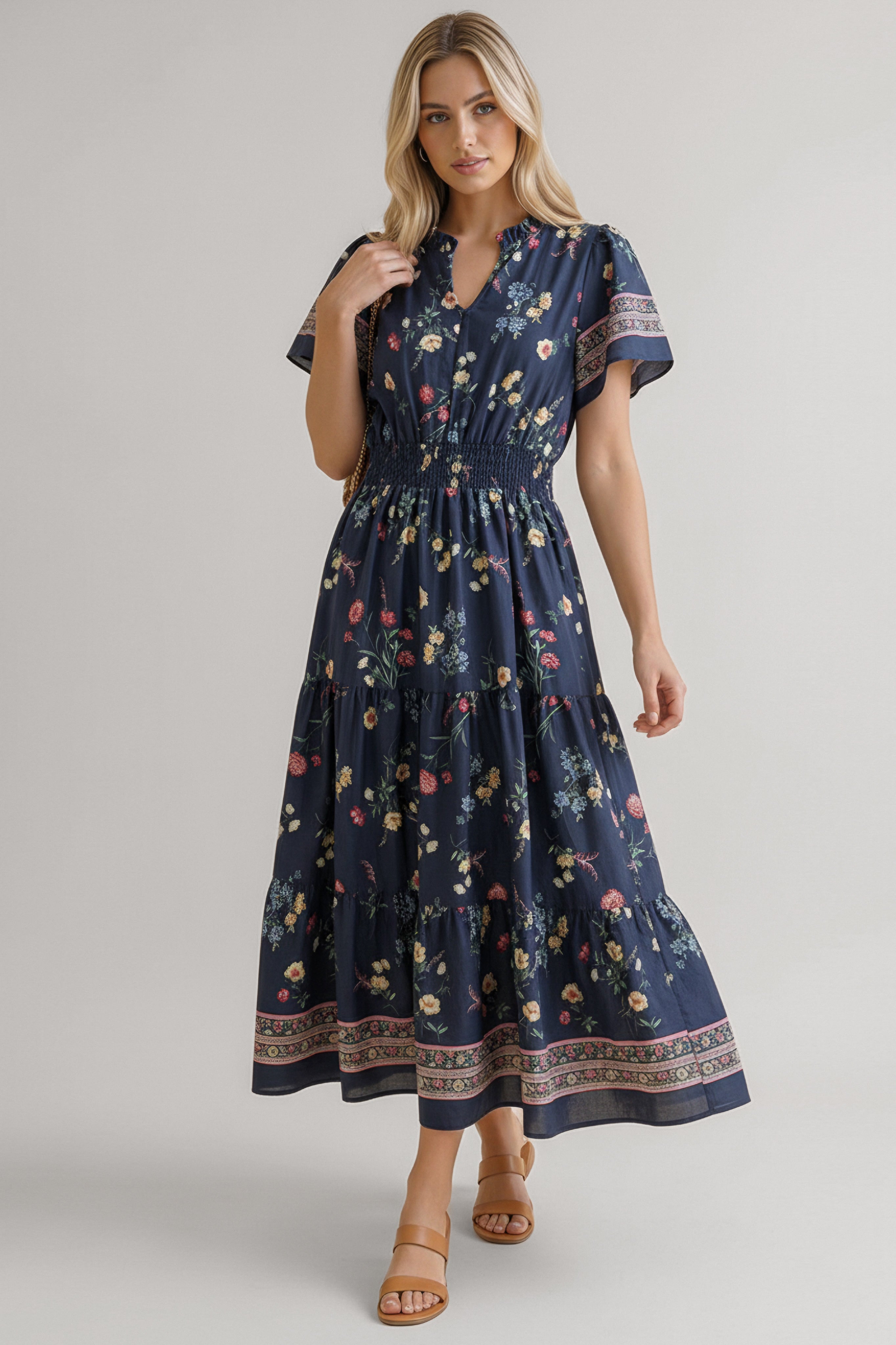 Blonde woman wearing a navy floral midi dress with short sleeves, smocked waist, and decorative border tiered skirt