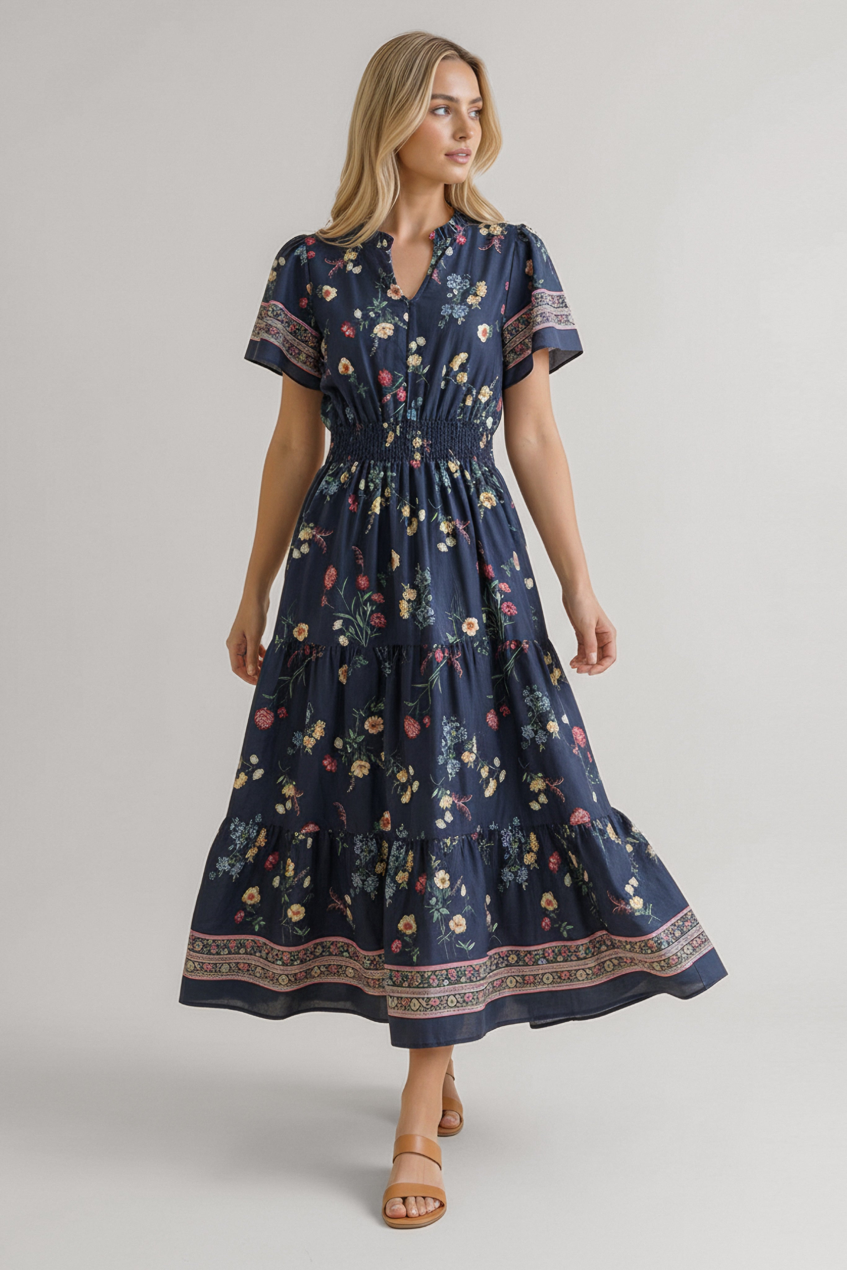 Woman wearing a navy floral midi dress with smocked waist, short sleeves, and decorative hem detail walking forward