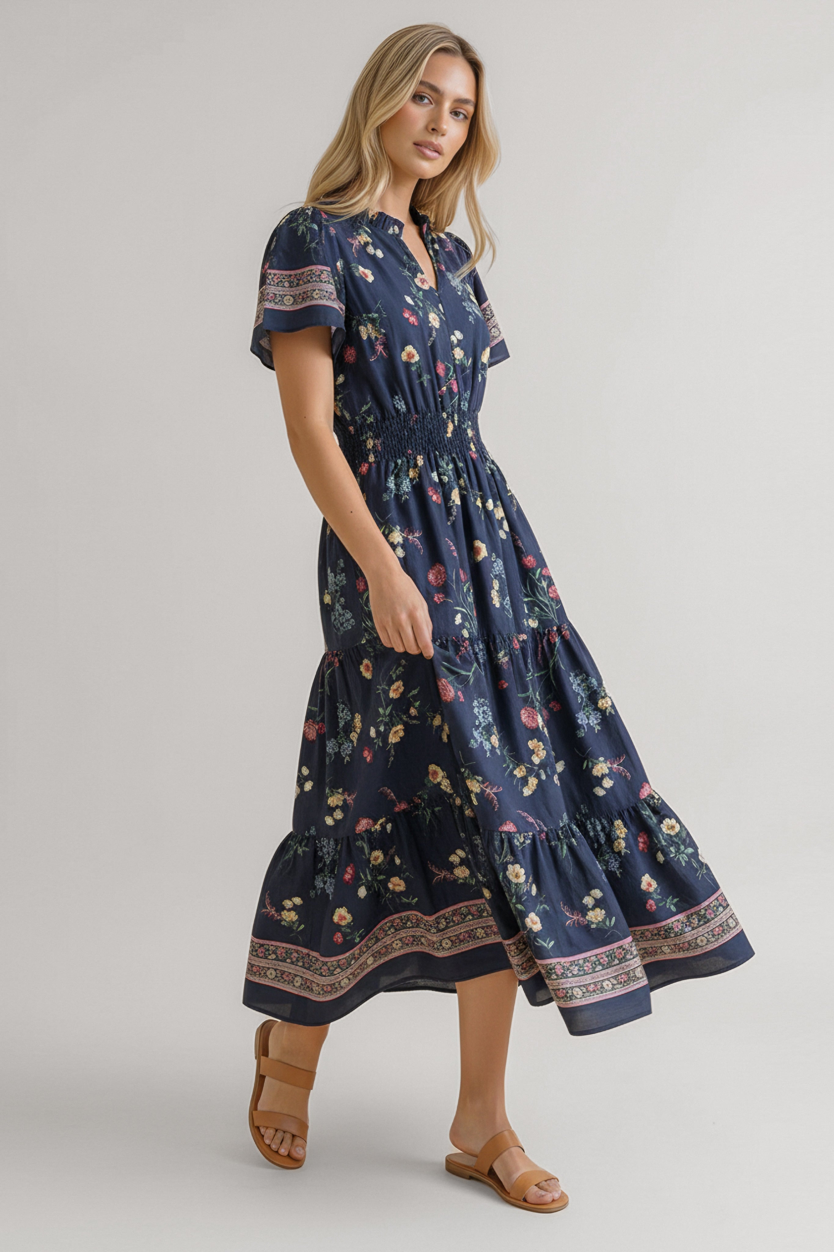 Woman wearing a navy floral midi dress with smocked waist, short sleeves, and patterned borders standing in profile