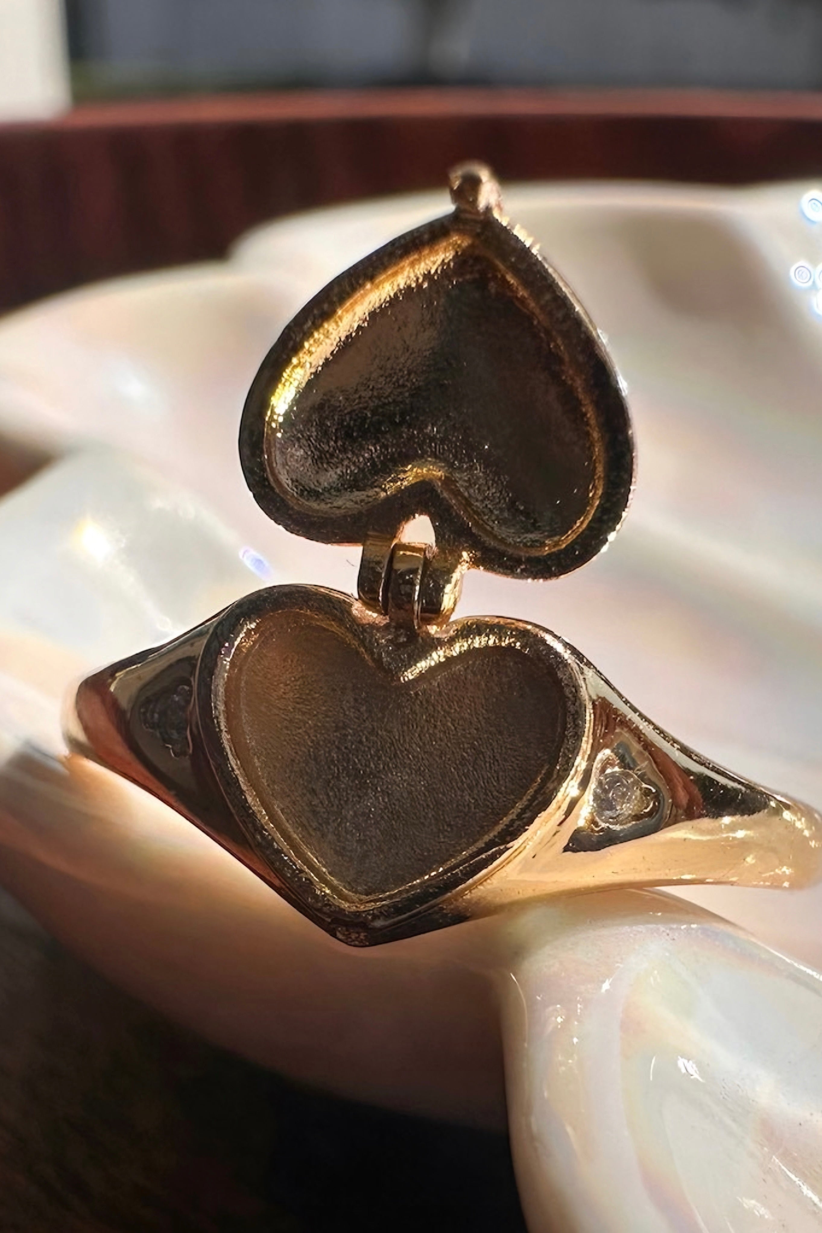 Open gold heart locket ring showing inner compartment with small diamond details on sides against blurred background