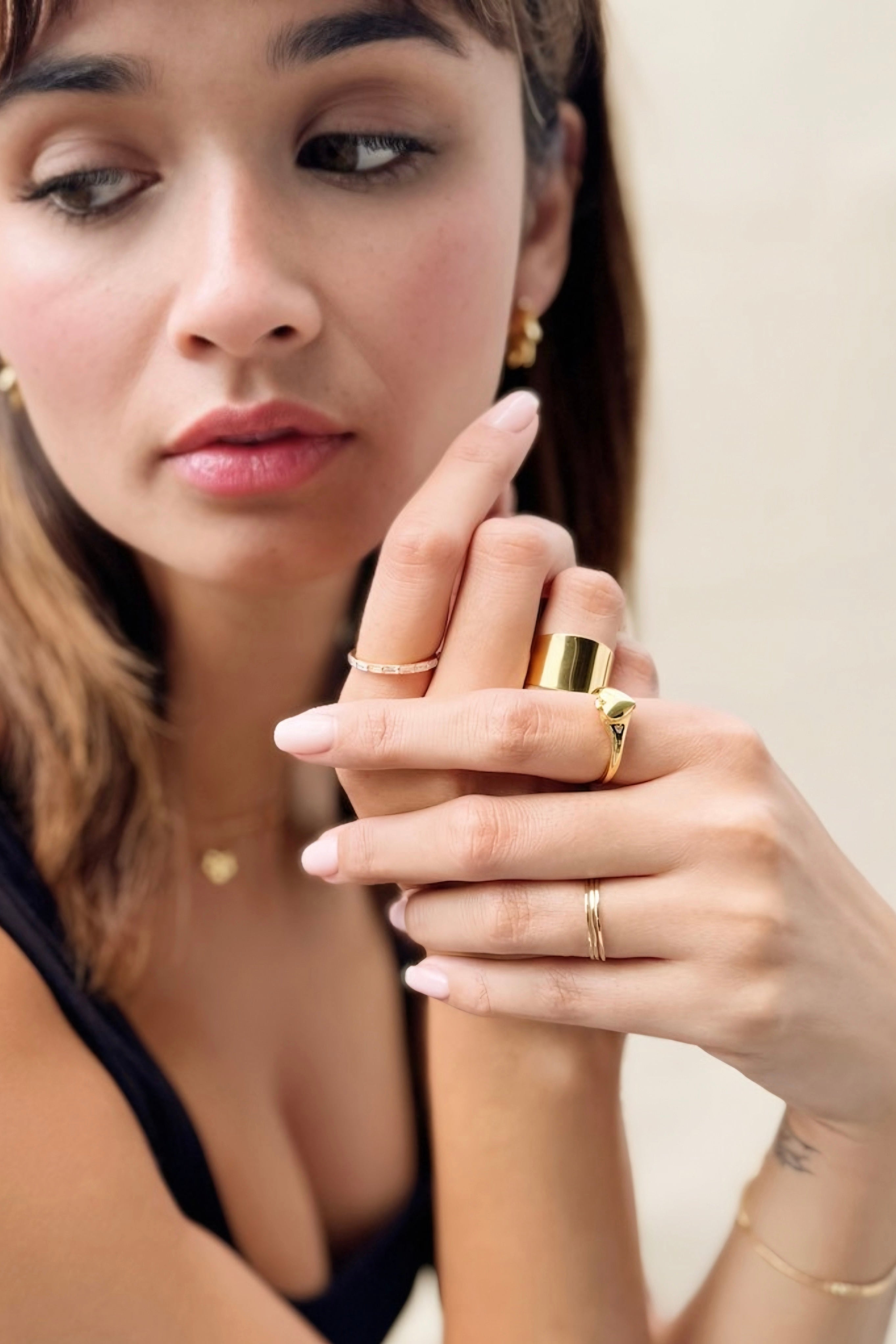 Model wearing Aurelia Heart Locket Ring on finger alongside other gold rings and delicate jewelry against neutral background