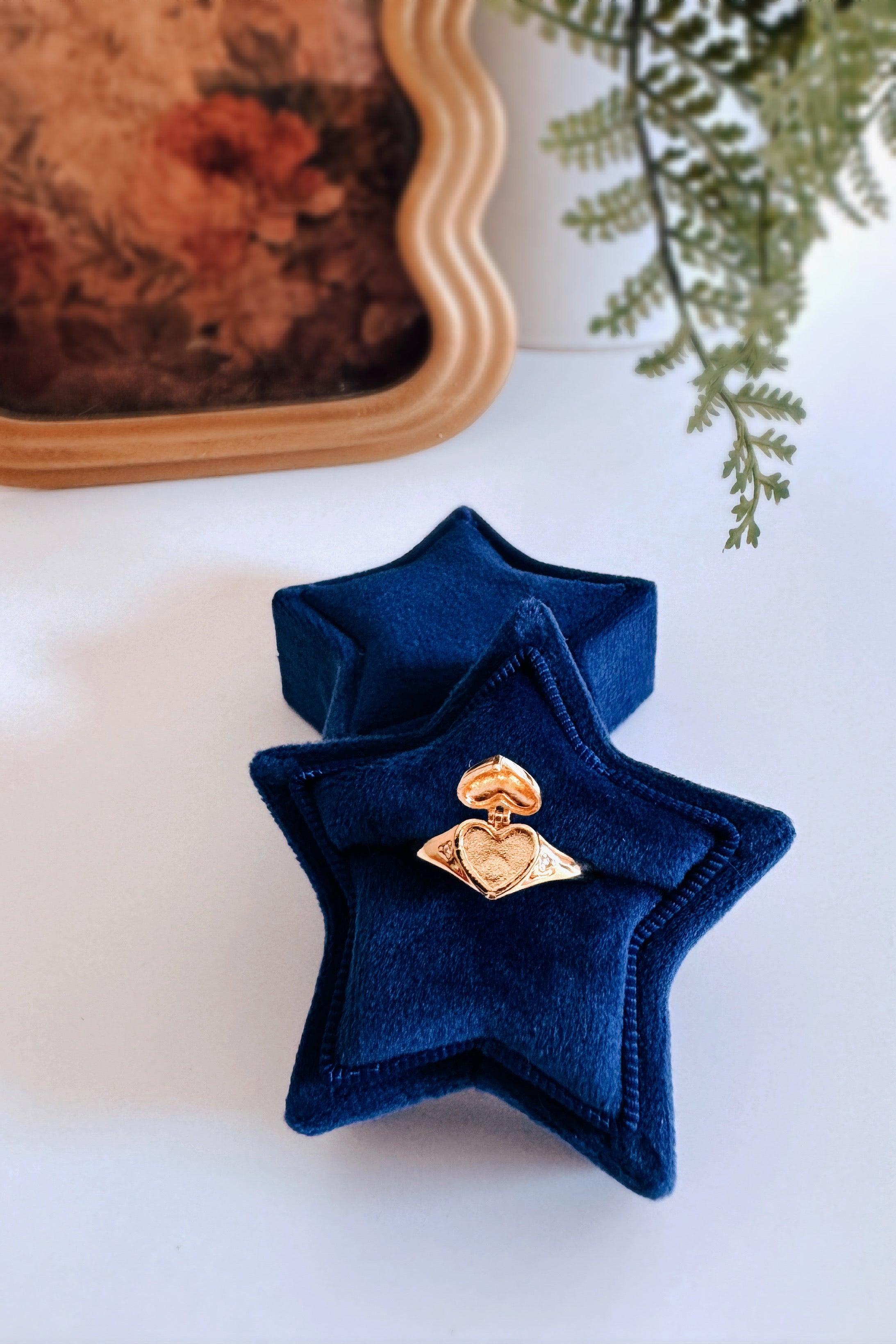 Gold Aurelia Heart Locket Ring displayed on navy blue velvet star-shaped ring box with soft floral and greenery accents