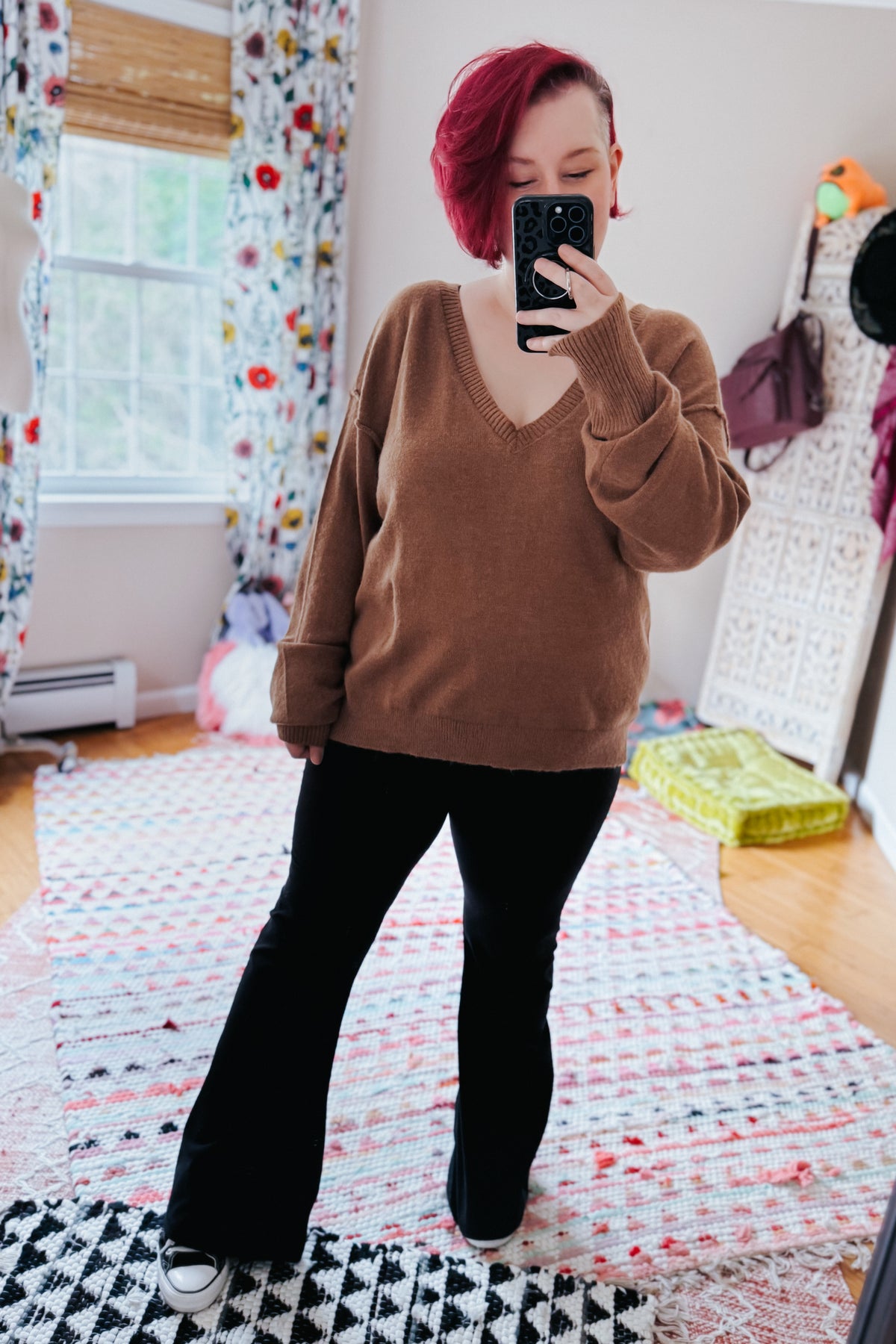 Mocha V-neck sweater with dropped shoulders and exposed seams styled with black flared pants in a casual mirror selfie