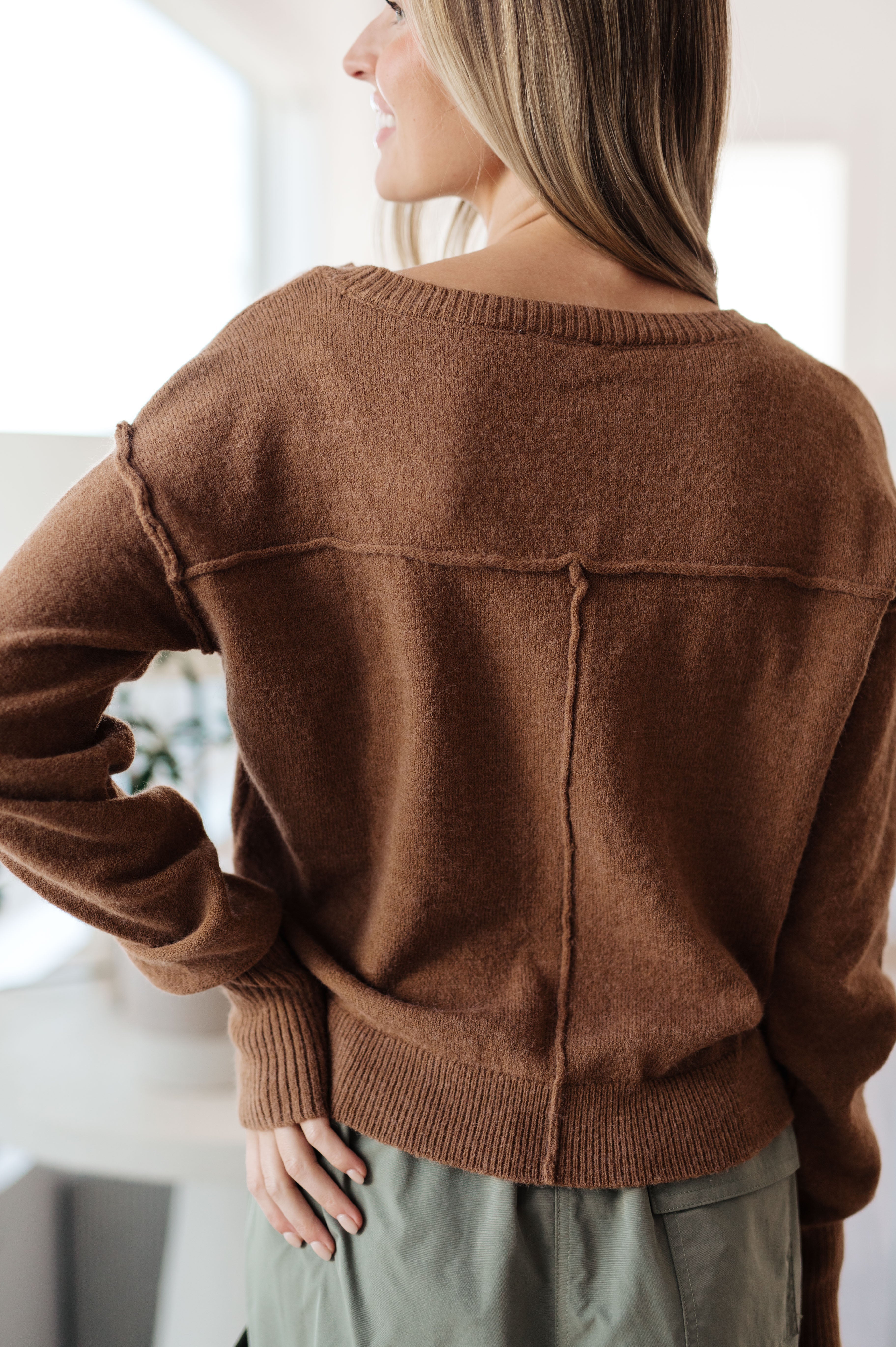Woman shown from behind wearing mocha-colored Back to Life V-Neck Sweater with visible seam details in soft light setting