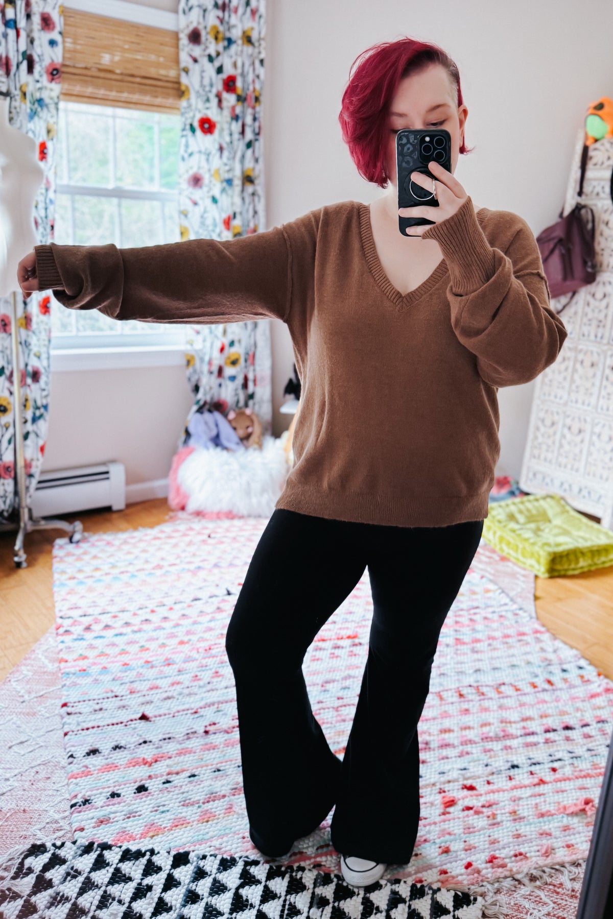 Mocha V neck sweater with dropped shoulders and exposed seams styled with black flared pants in a cozy bedroom