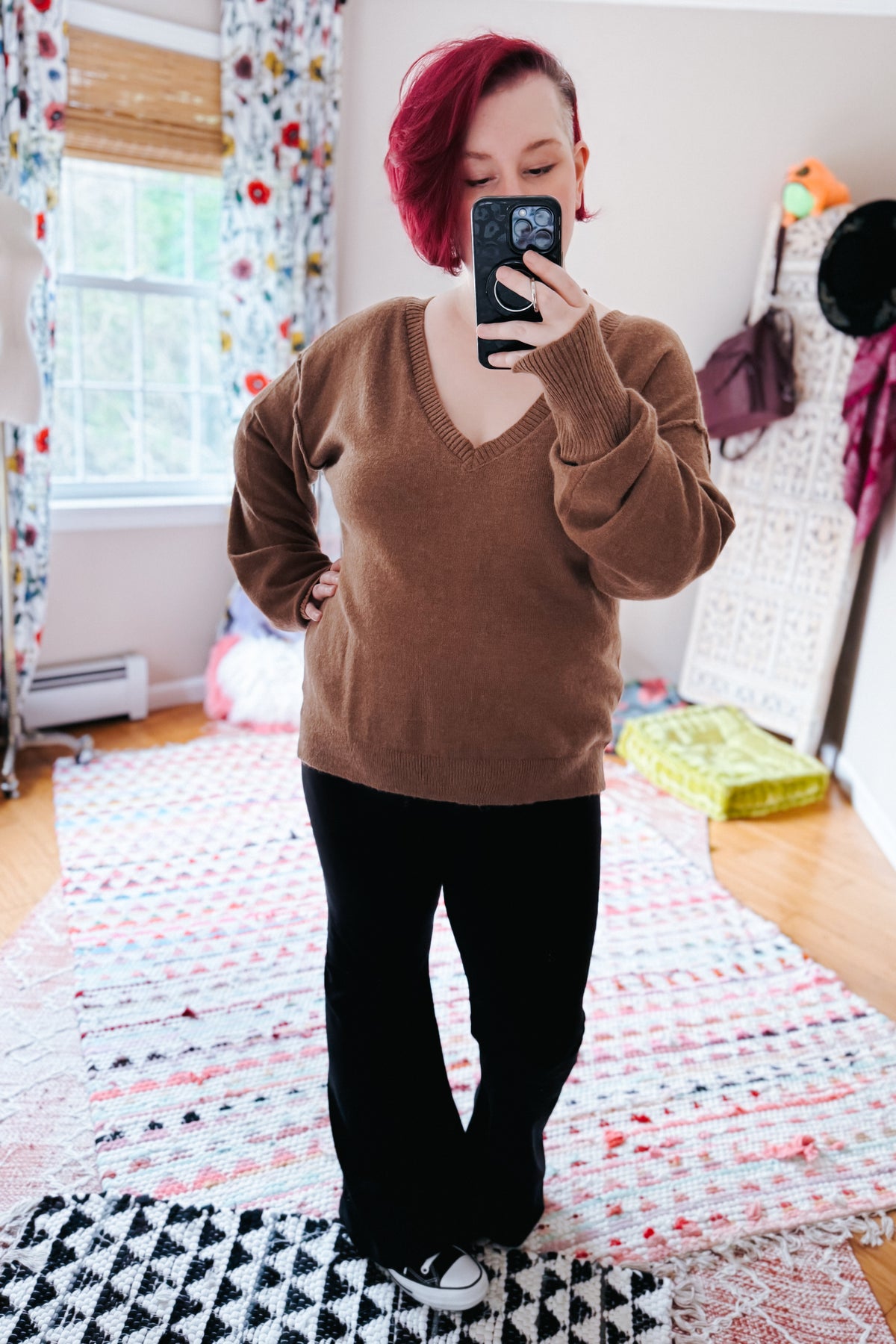 Mocha V neck sweater with dropped shoulders and exposed seams styled with black pants in a colorful bedroom mirror selfie