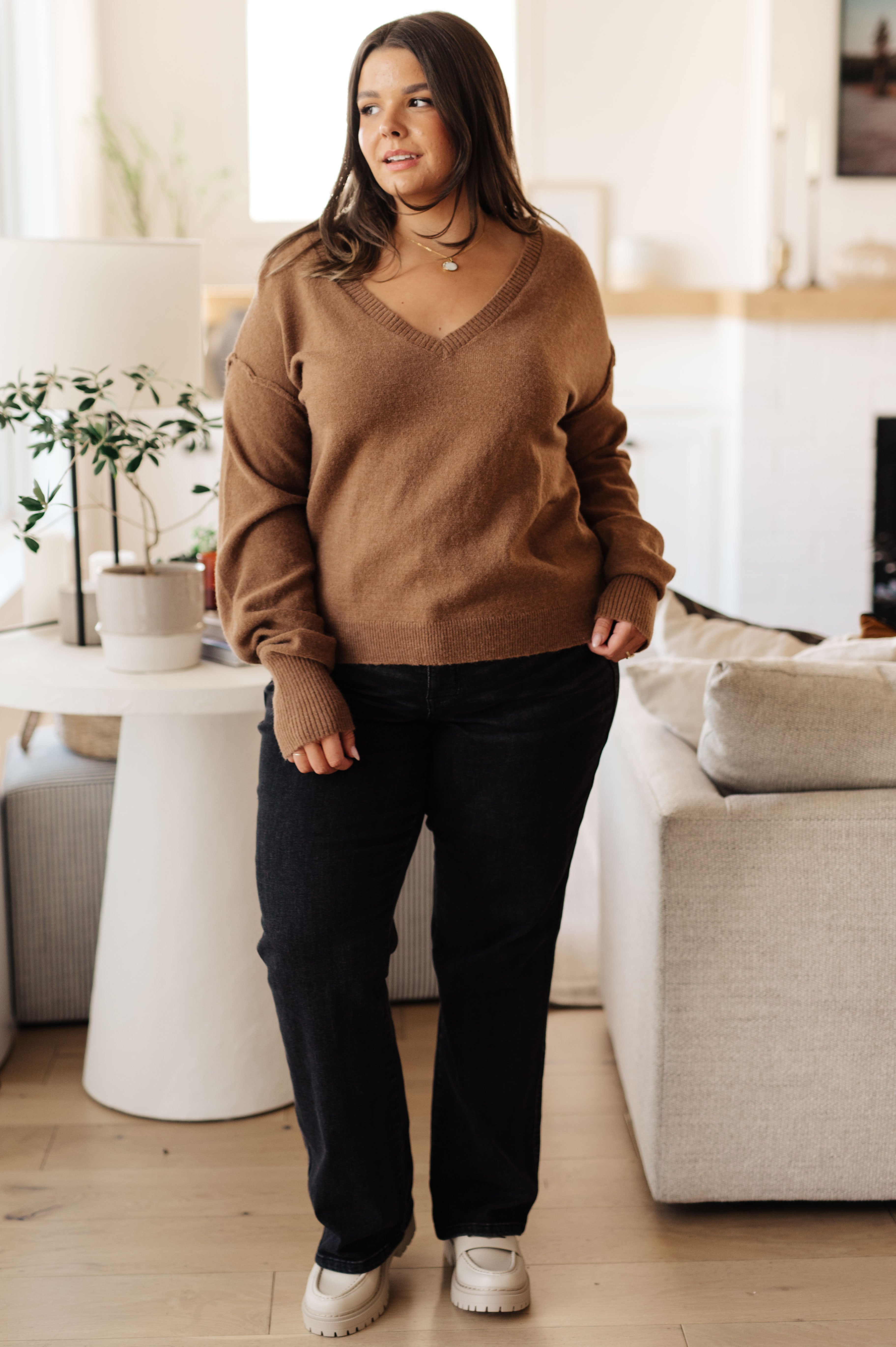 Woman wearing mocha Back to Life V-Neck Sweater with ribbed cuffs, relaxed fit, standing in cozy living room, full front view