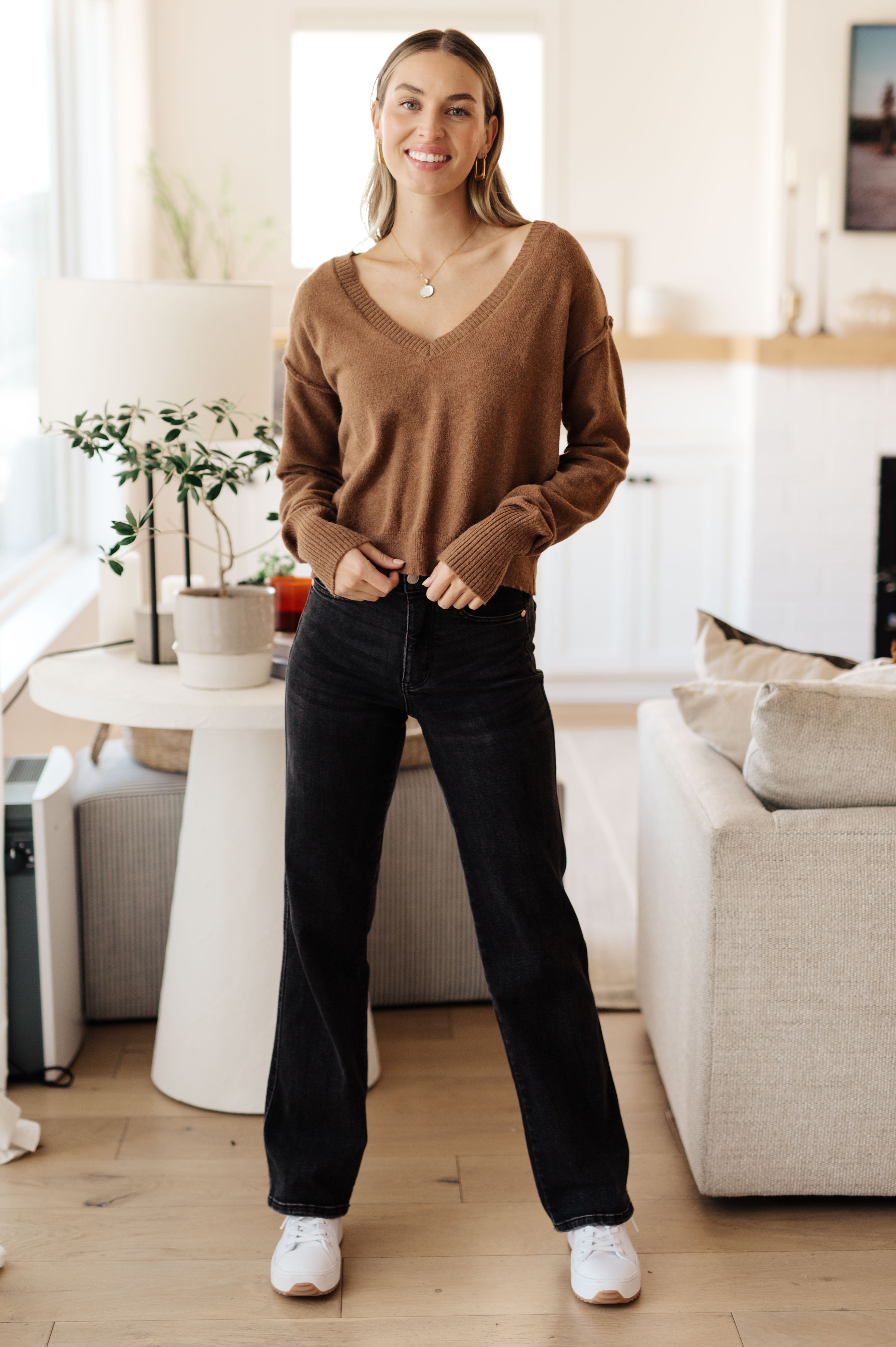 Woman wearing mocha Back to Life V-Neck Sweater with ribbed cuffs standing in cozy living room, full front view