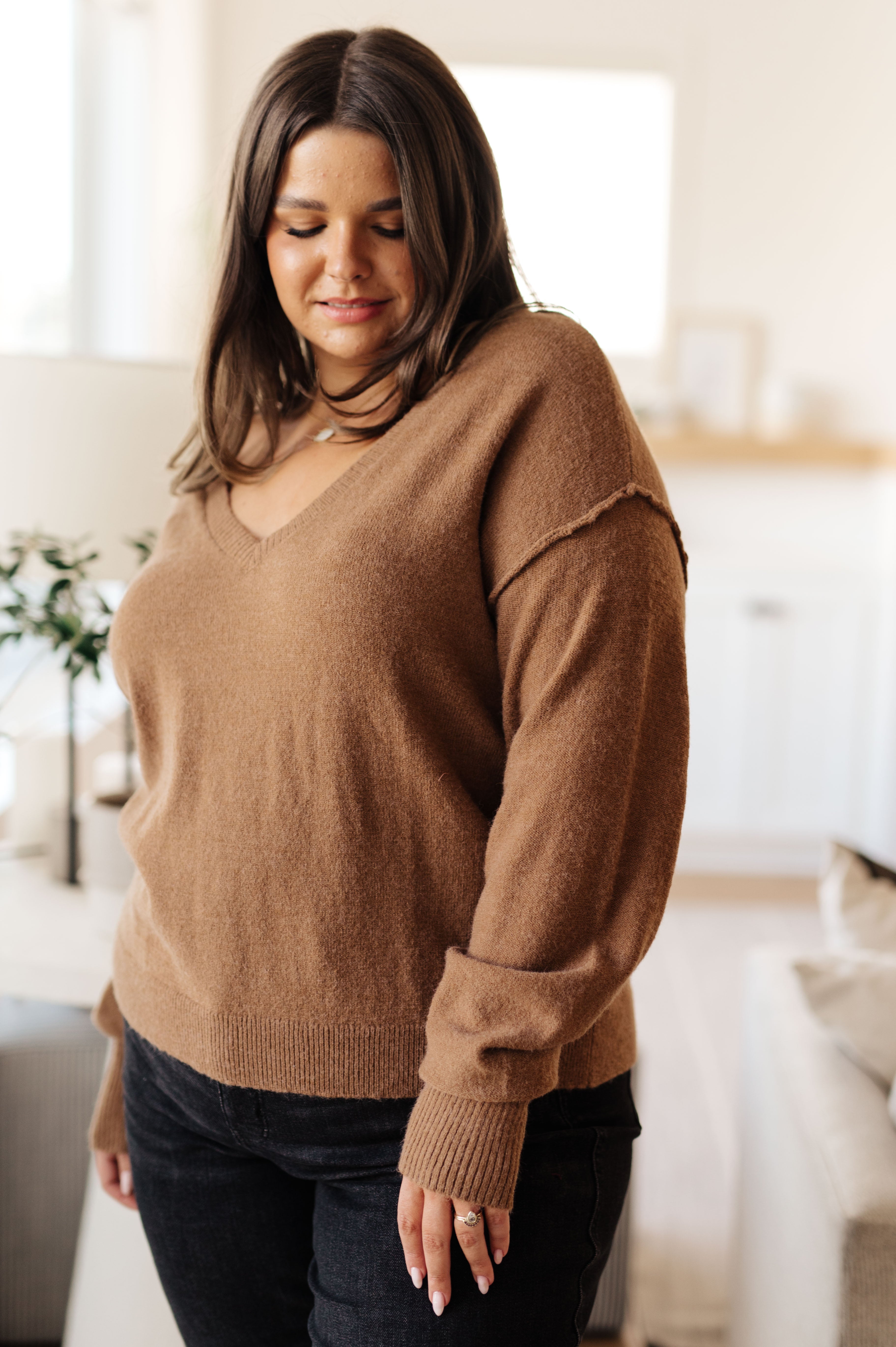 Plus size woman wearing mocha Back to Life V-Neck Sweater with relaxed fit and dropped shoulder seam in bright living room