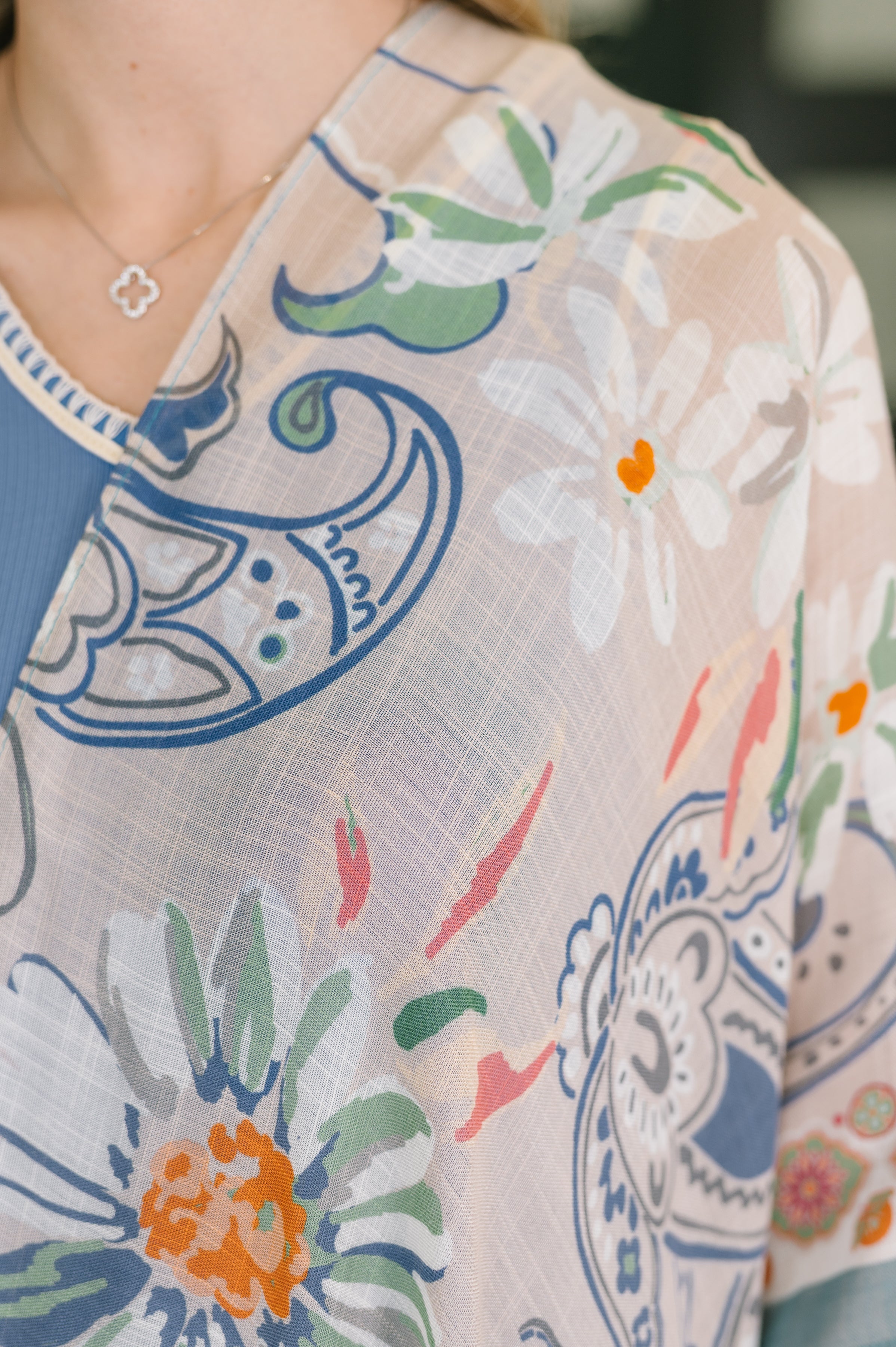 Close-up of lightweight sheer layering piece with colorful floral and paisley print worn over blue garment and silver necklace