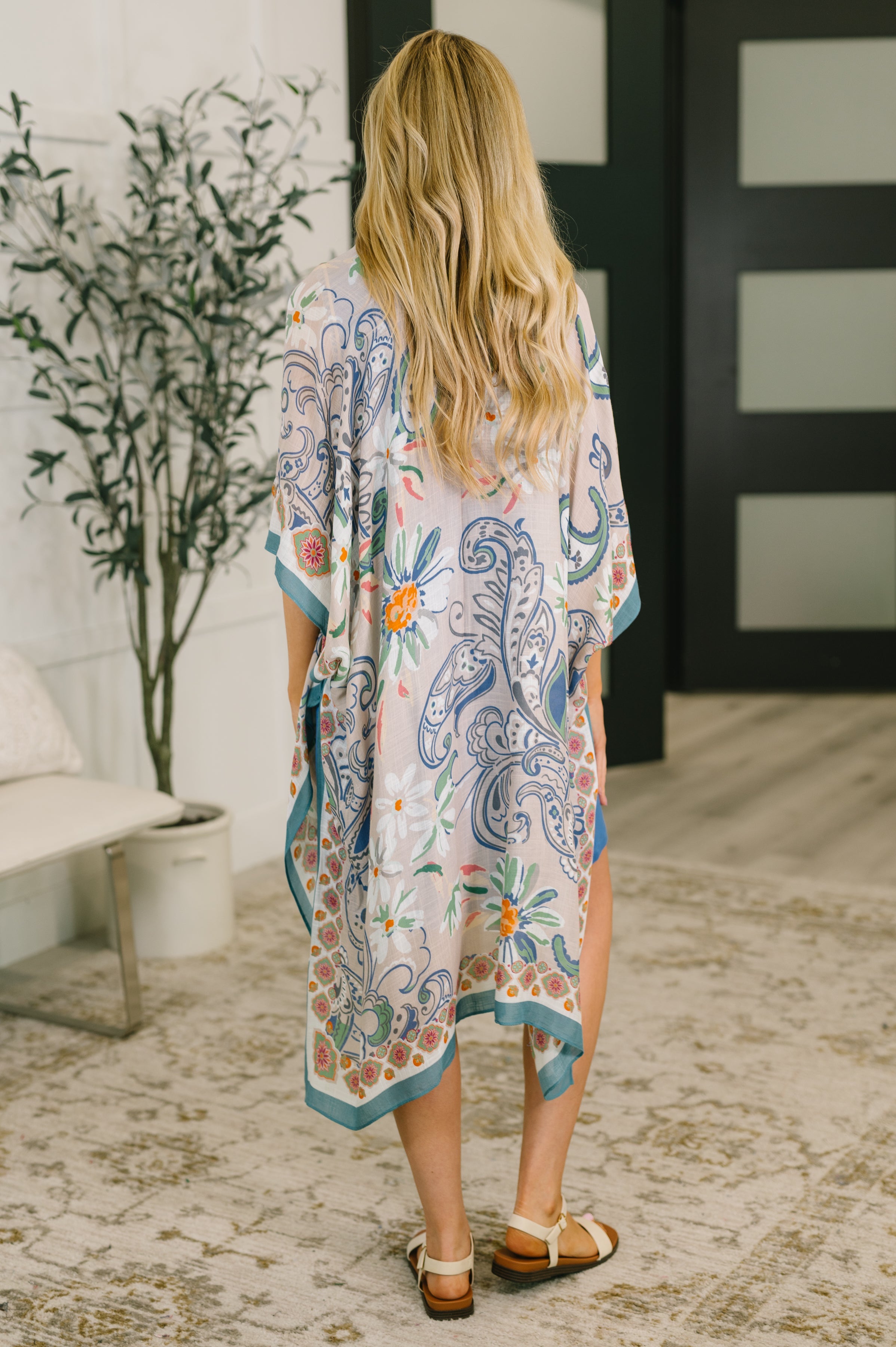 Woman wearing lightweight layering piece with blue paisley and floral print standing indoors on patterned rug
