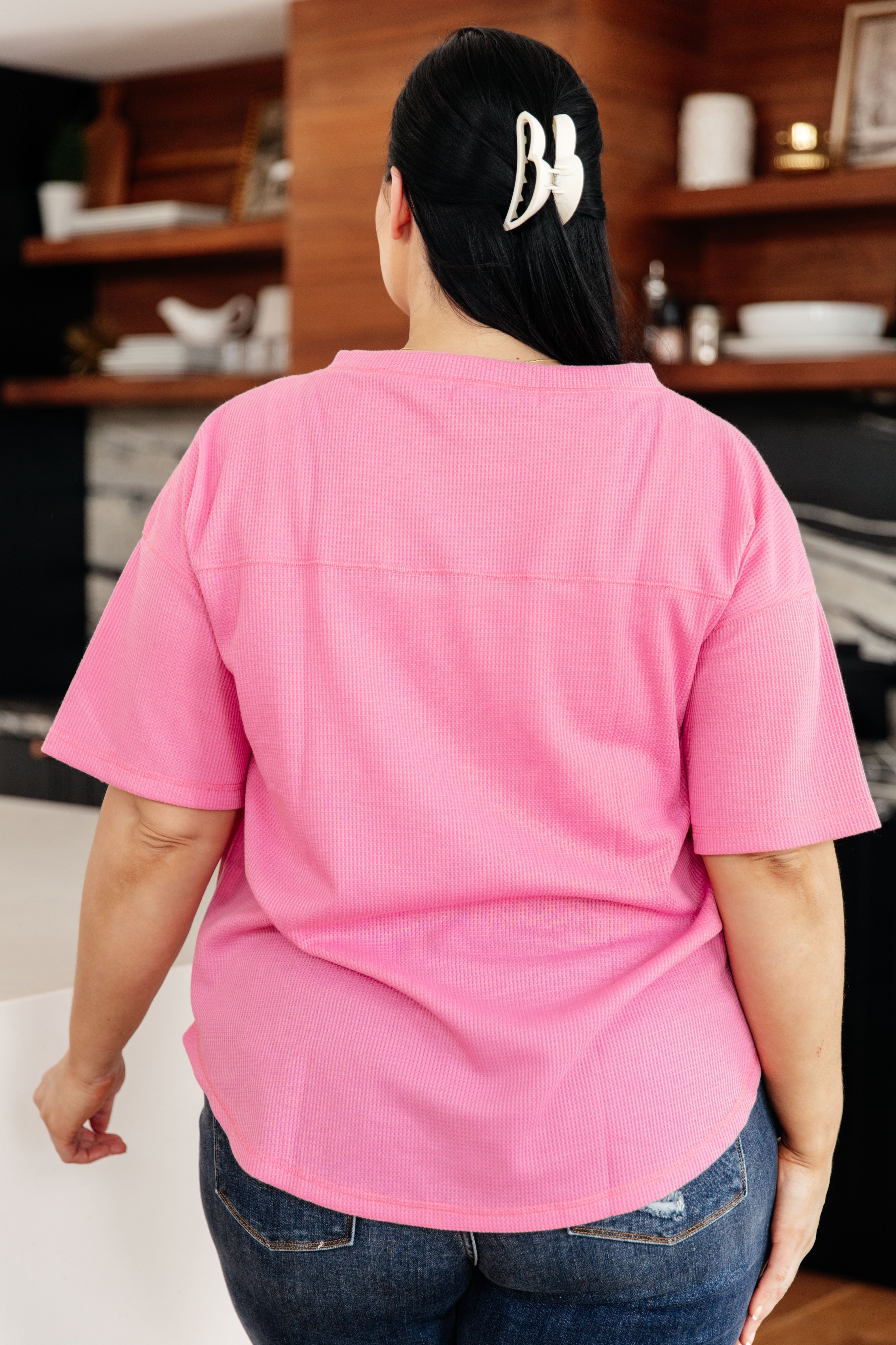Plus size woman seen from behind wearing pink Back Together V-Neck Top, short sleeves, paired with distressed blue jeans indoors