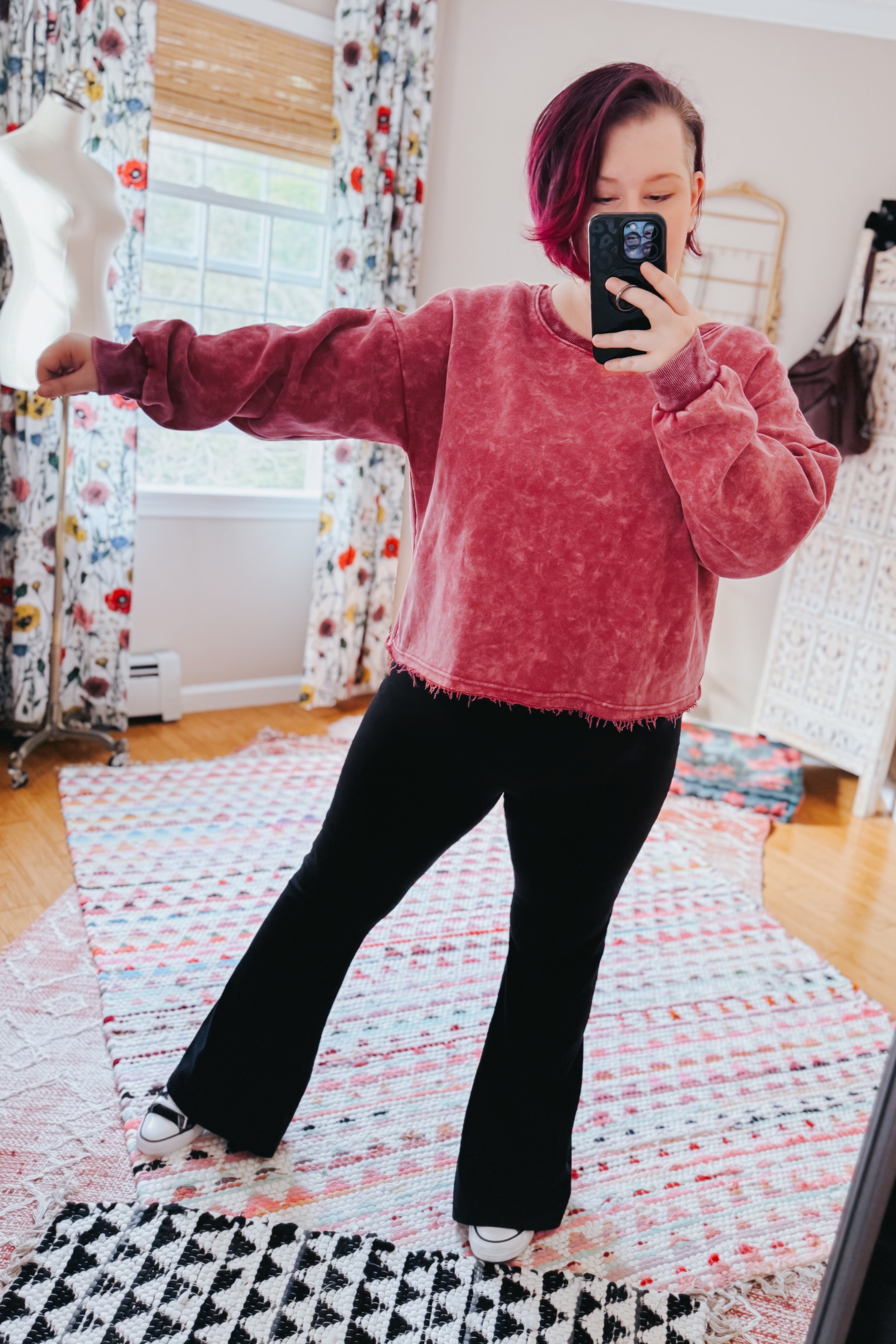 Person with short magenta hair wearing Bad Company Acid Wash Cropped Pullover in berry, posing with arm extended indoors