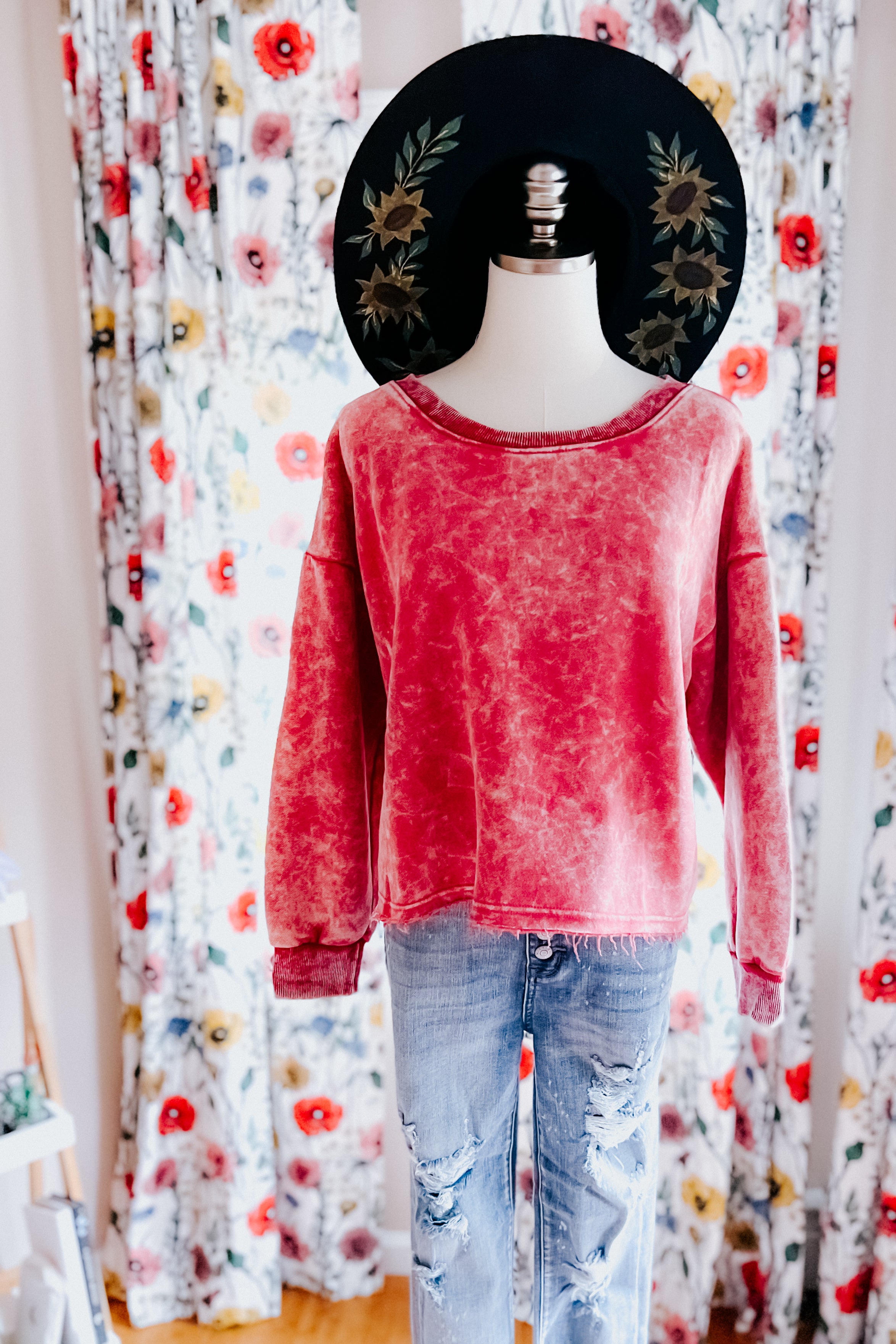 Mannequin wearing berry acid wash cropped pullover with distressed hem paired with ripped light blue jeans in front of floral curtains