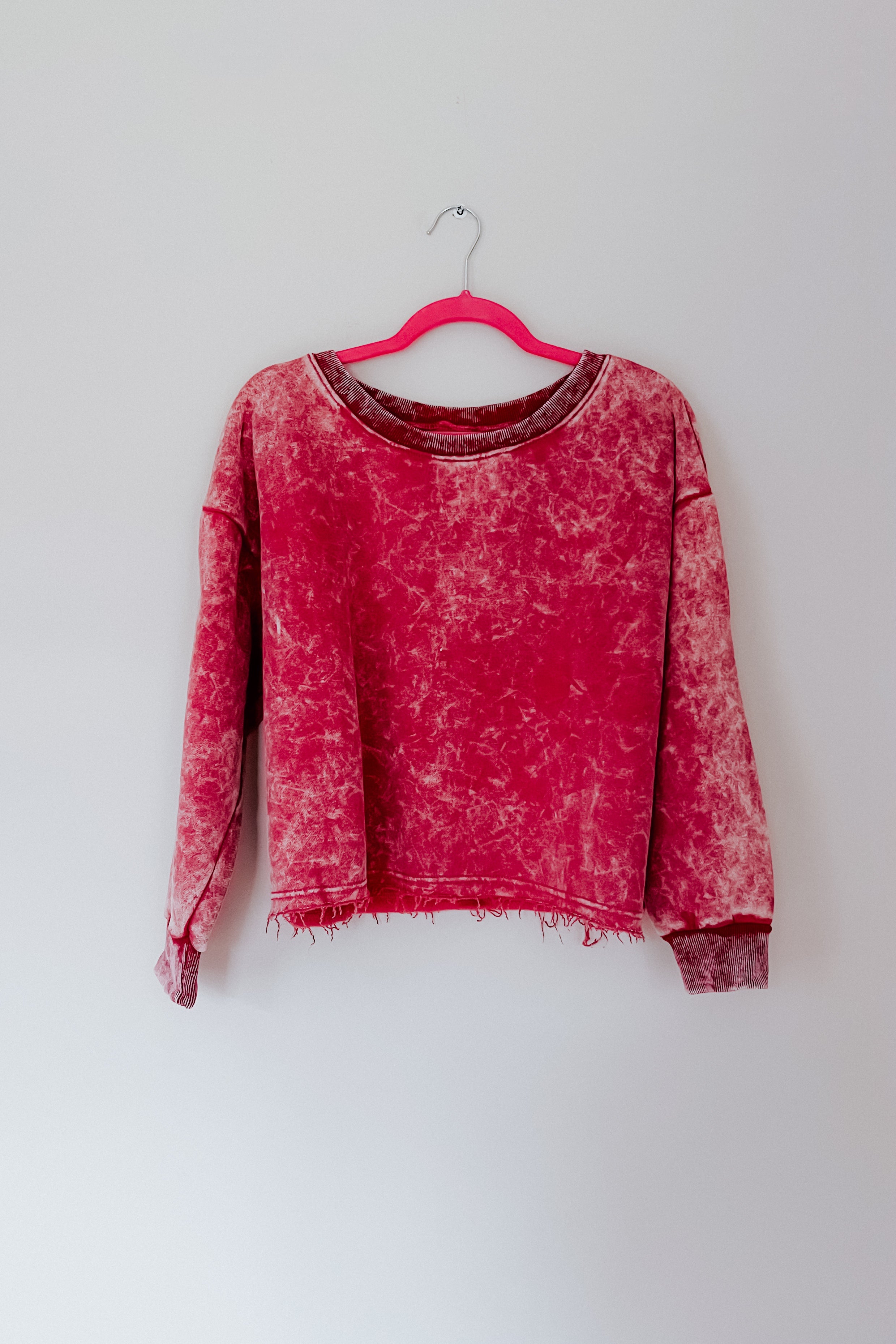 Berry-colored acid wash cropped pullover hanging on pink hanger against plain white wall, gallery image 0