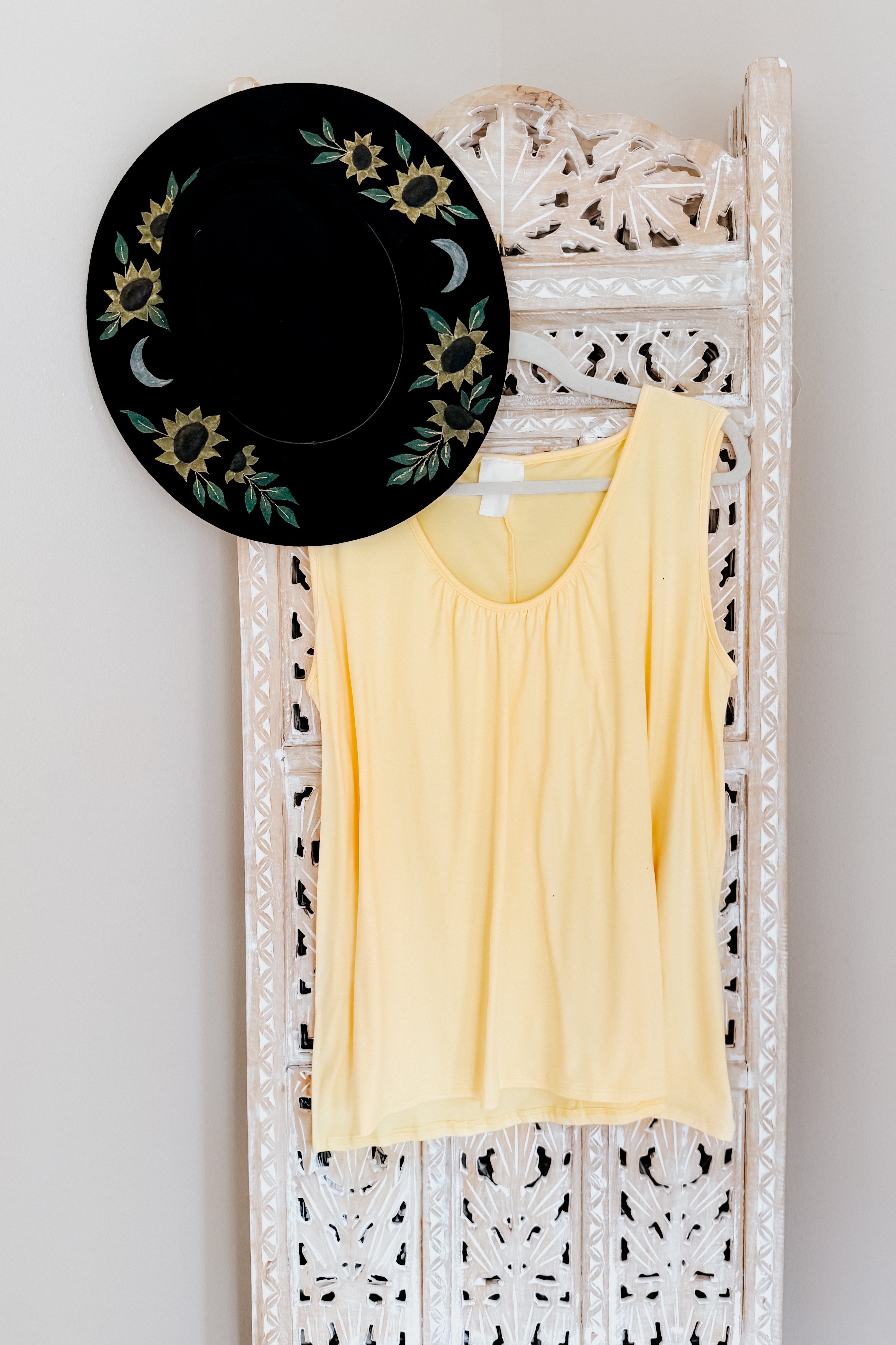 Pale yellow Banana Bliss tank top with scoop neck hanging on carved wooden panel with black sunflower hat above