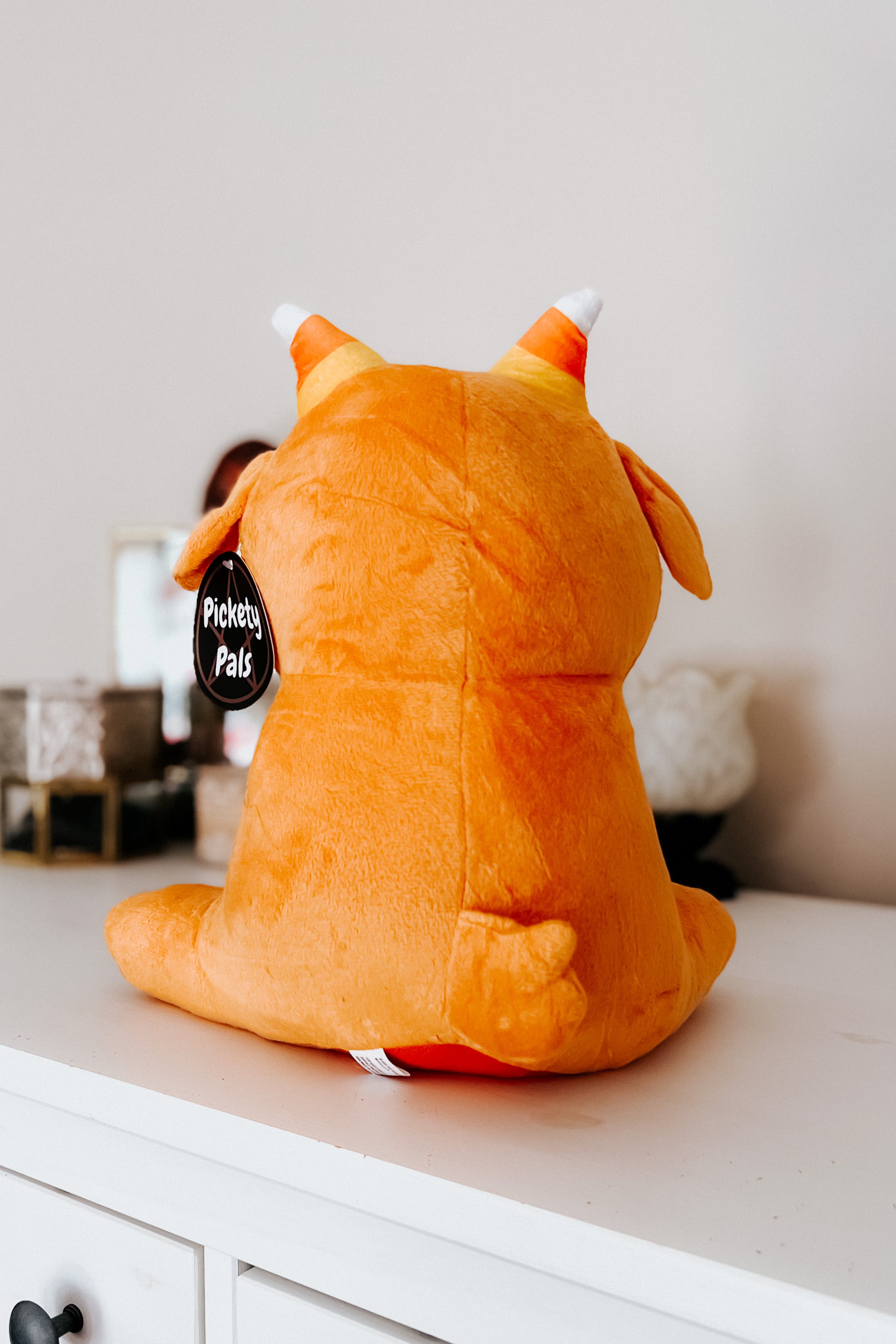 Back view of pumpkin spice Baphy Witchy Baby Goat plush with small tail and candy corn striped horns on white dresser